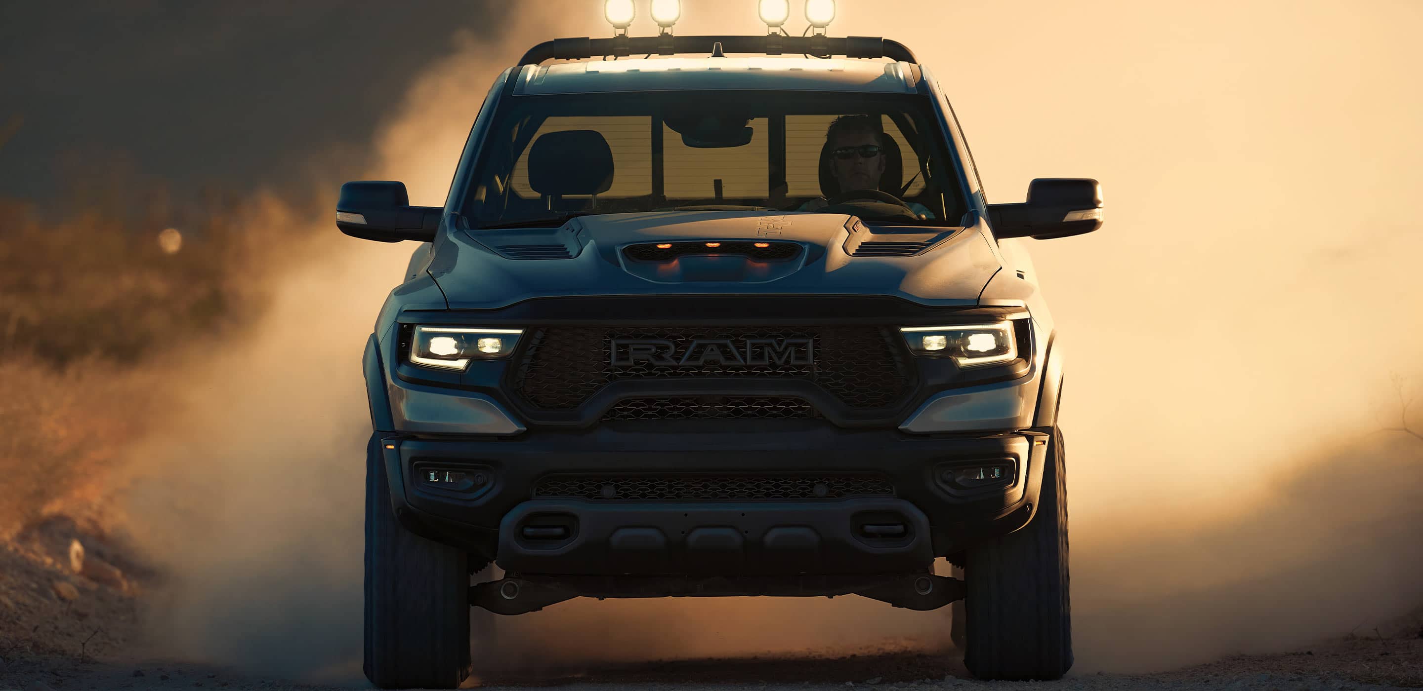 The front of a 2022 Ram 1500 with a man driving it on the dirt