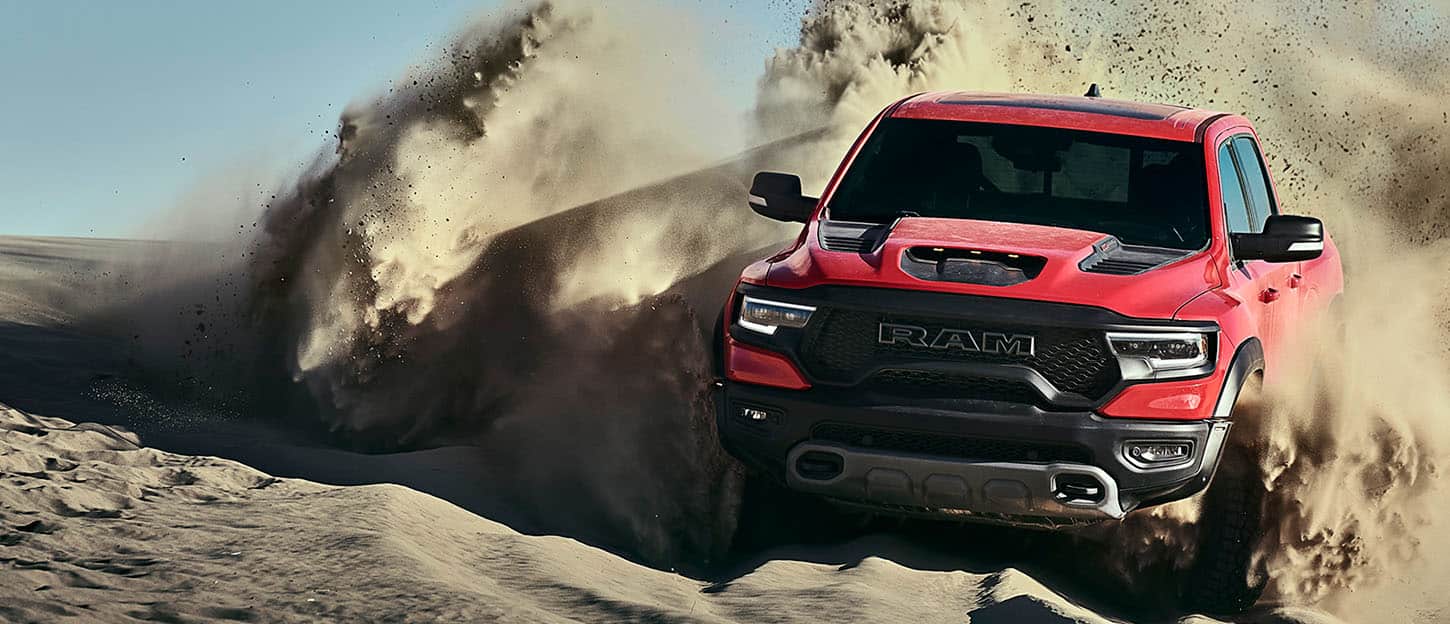 The 2022 Ram TRX surrounded by a large dust cloud as it's driven over a sand dune.