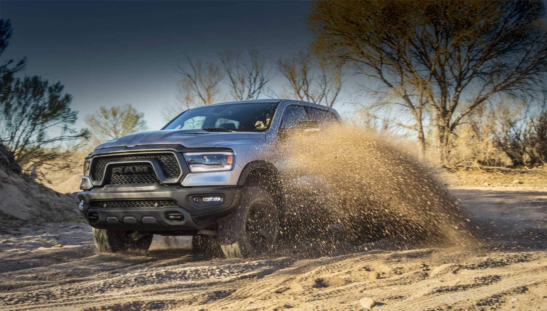 The 2023 Ram 1500 being driven off-road on sand, a cloud of dust coming from its wheels.