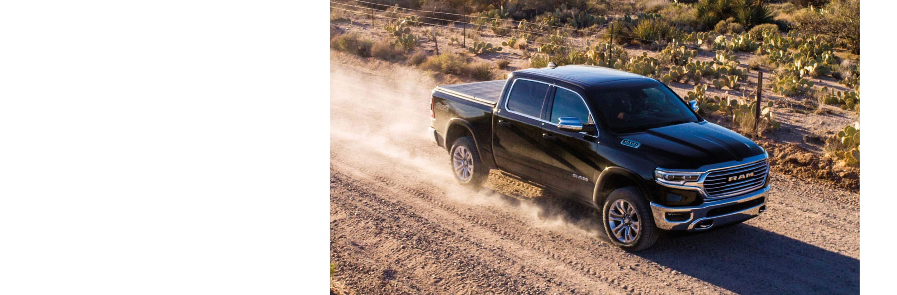 The 2023 Ram 1500 being driven on a dirt road past fenced-off crops.