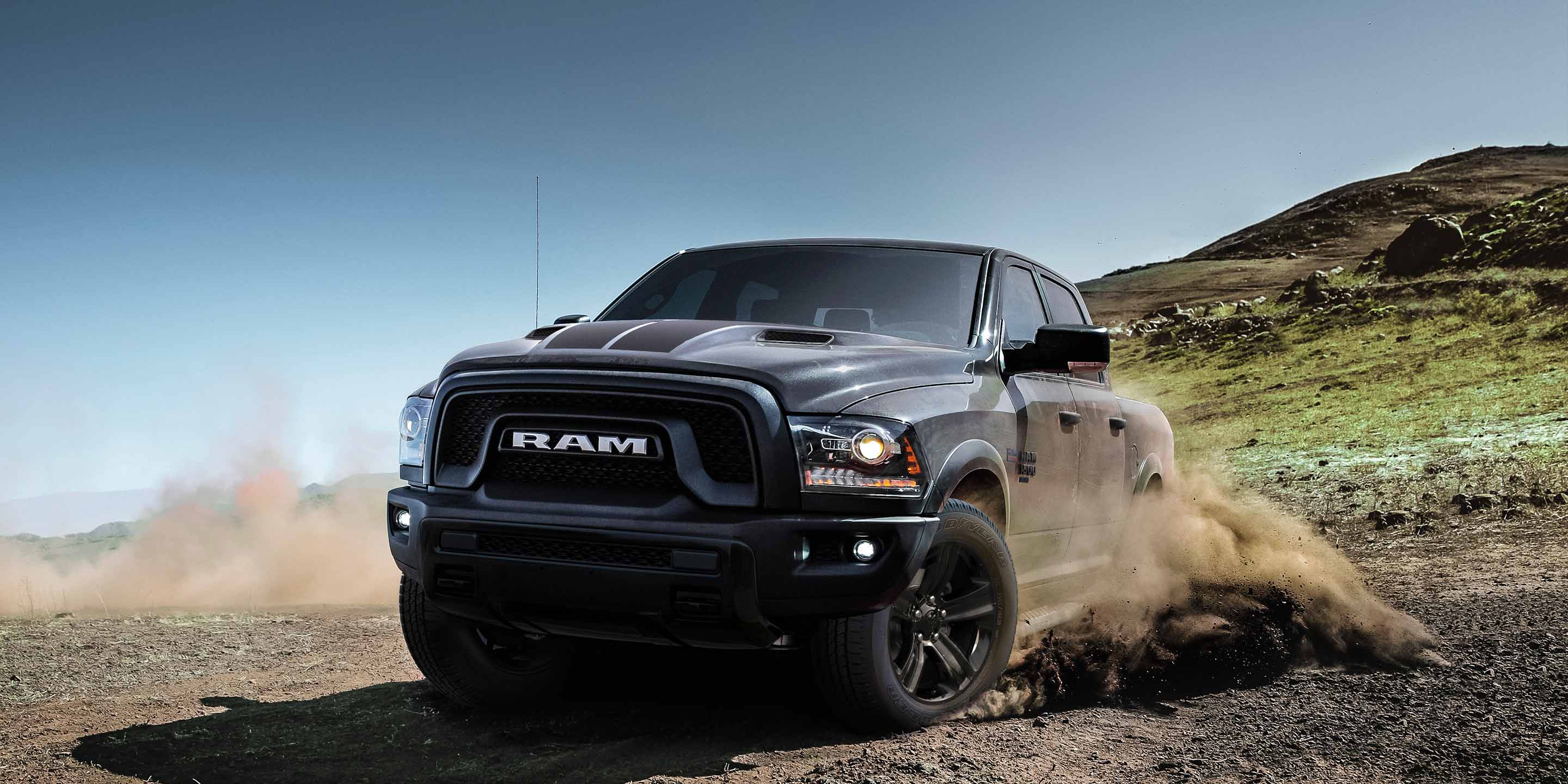 A gray 2023 Ram 1500 Classic TBD Crew Cab being driven off-road down a hill, kicking up dust in its wake.