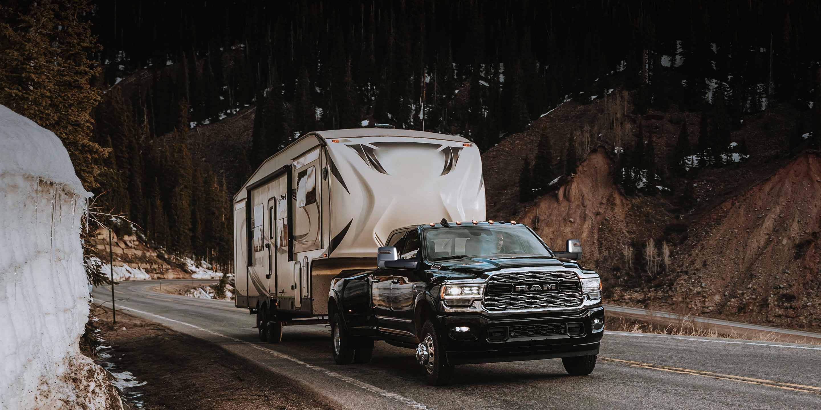 A 2023 Ram 3500 Limited Crew Cab towing a fifth wheel travel trailer as it is driven down a winding mountain road.