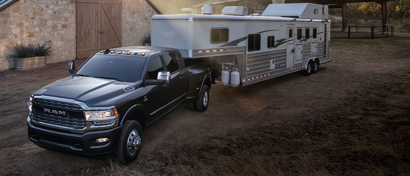 A 2023 Ram 3500 Limited Crew Cab towing a large covered trailer as it is driven down a highway in the rain.