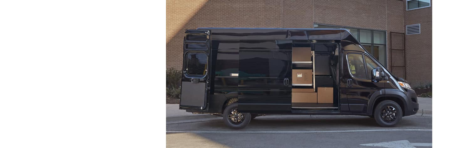 A 2023 Ram ProMaster with its side door open to reveal shelving upfits stacked with cardboard boxes.
