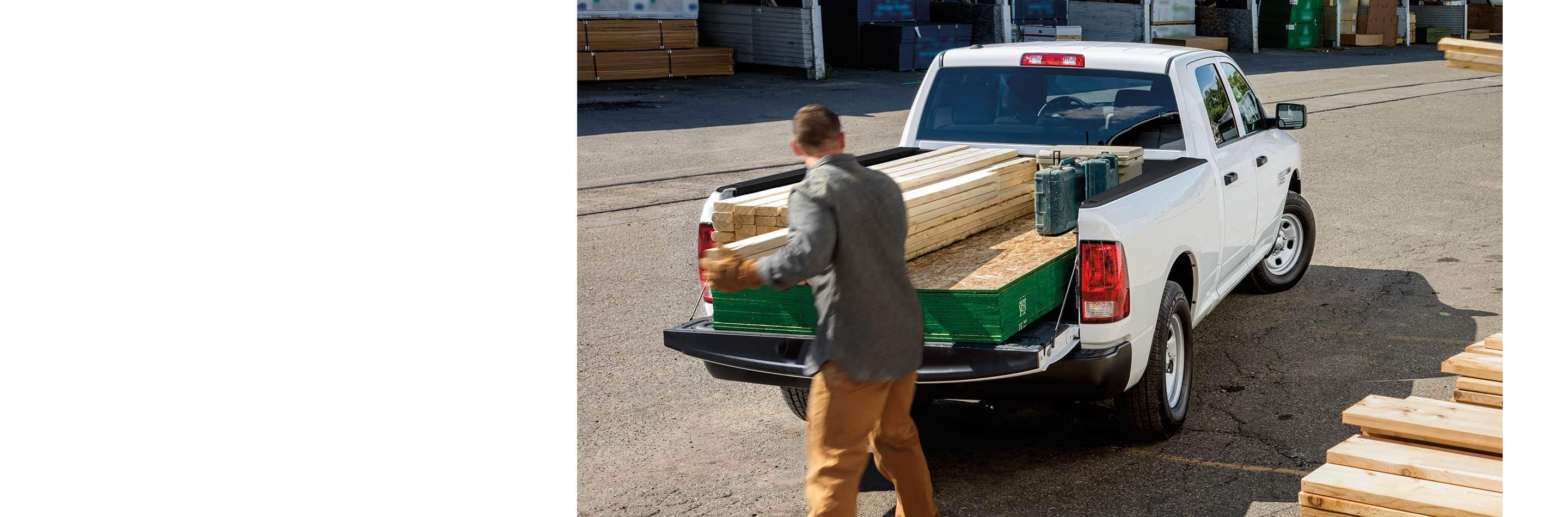 A man loading lumber into the pickup bed of a 2023 Ram 1500 Tradesman 4x4 Quad Cab.