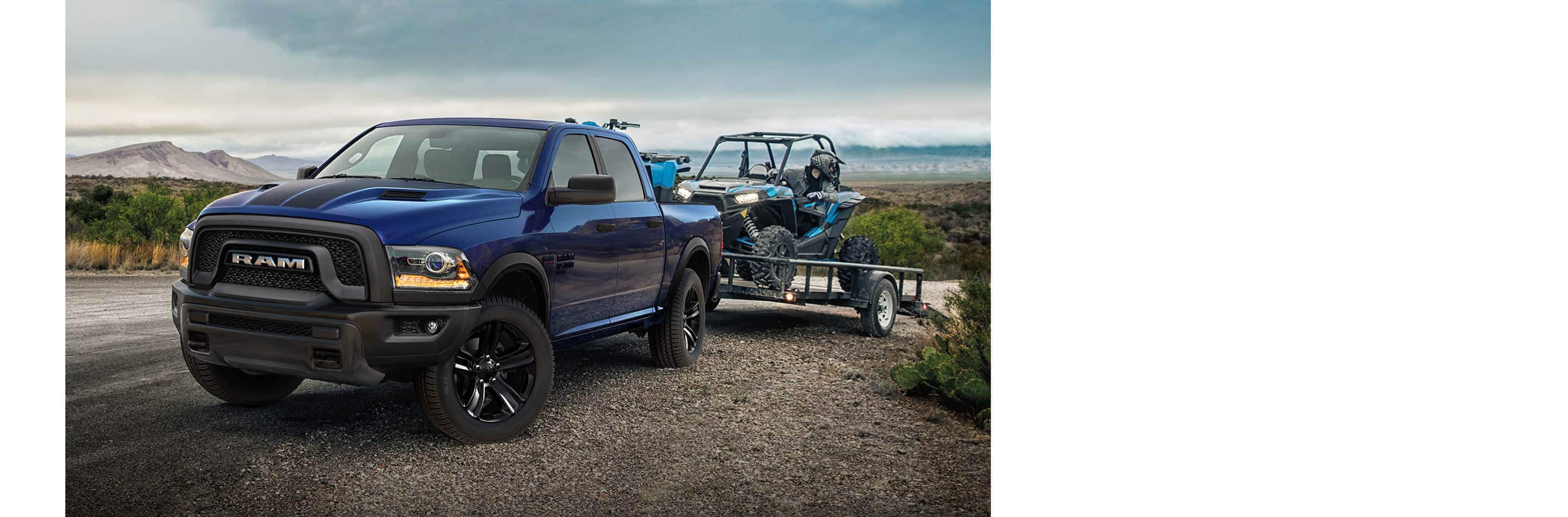 A blue 2023 Ram 1500 Classic Warlock 4x4 Crew Cab hitched to a flatbed trailer with an ATV on it.
