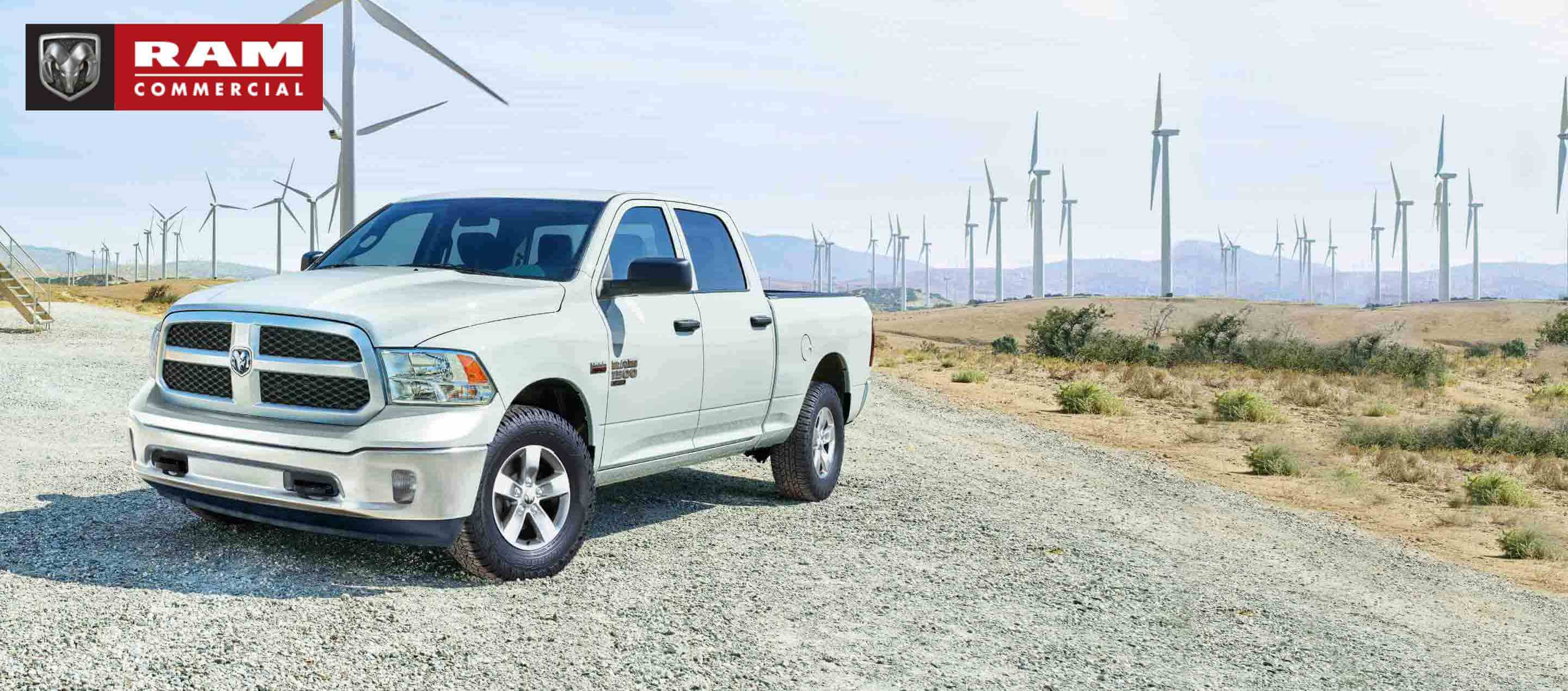 A white 2023 Ram 1500 Classic Tradesman Crew Cab parked beside a field of windmills. Ram Commercial.
