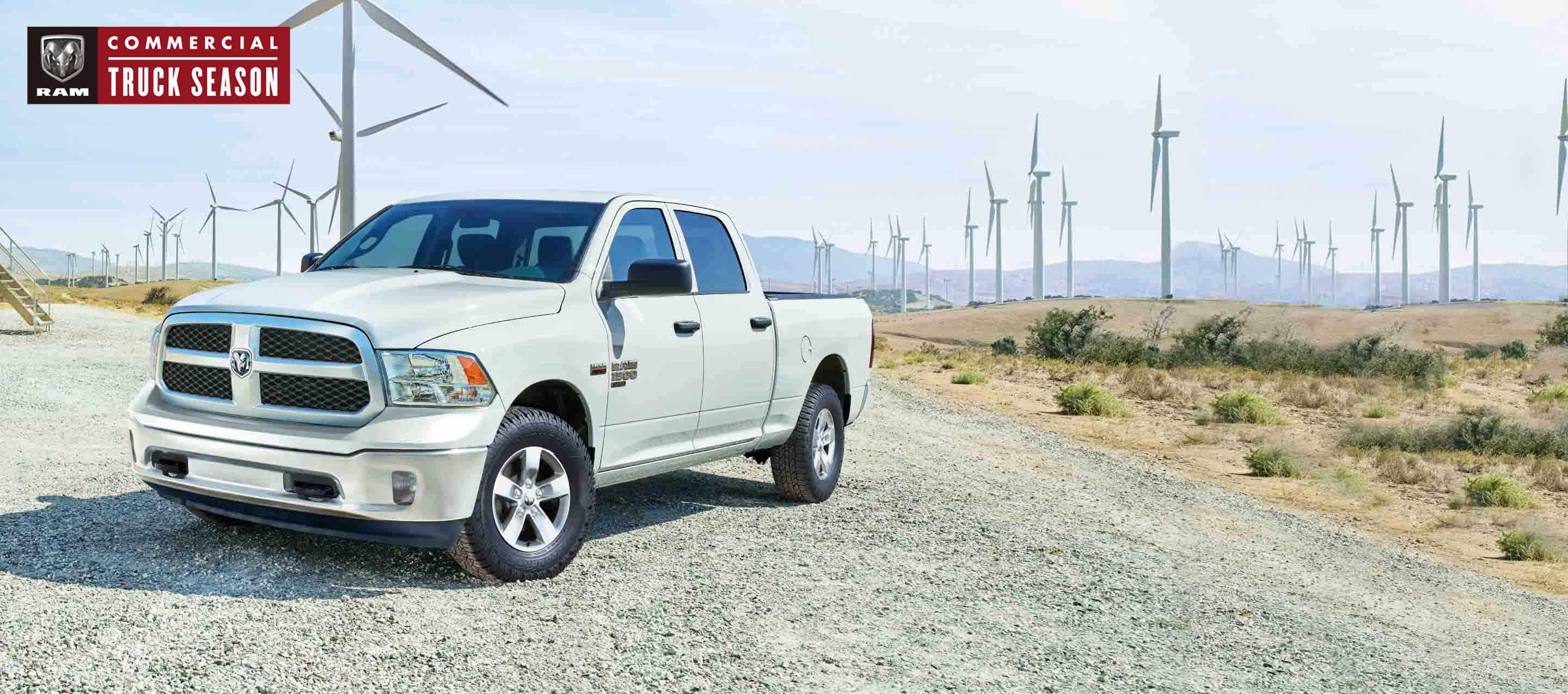 A white 2023 Ram 1500 Classic Tradesman Crew Cab parked beside a field of windmills. Ram Commercial Truck Season.
