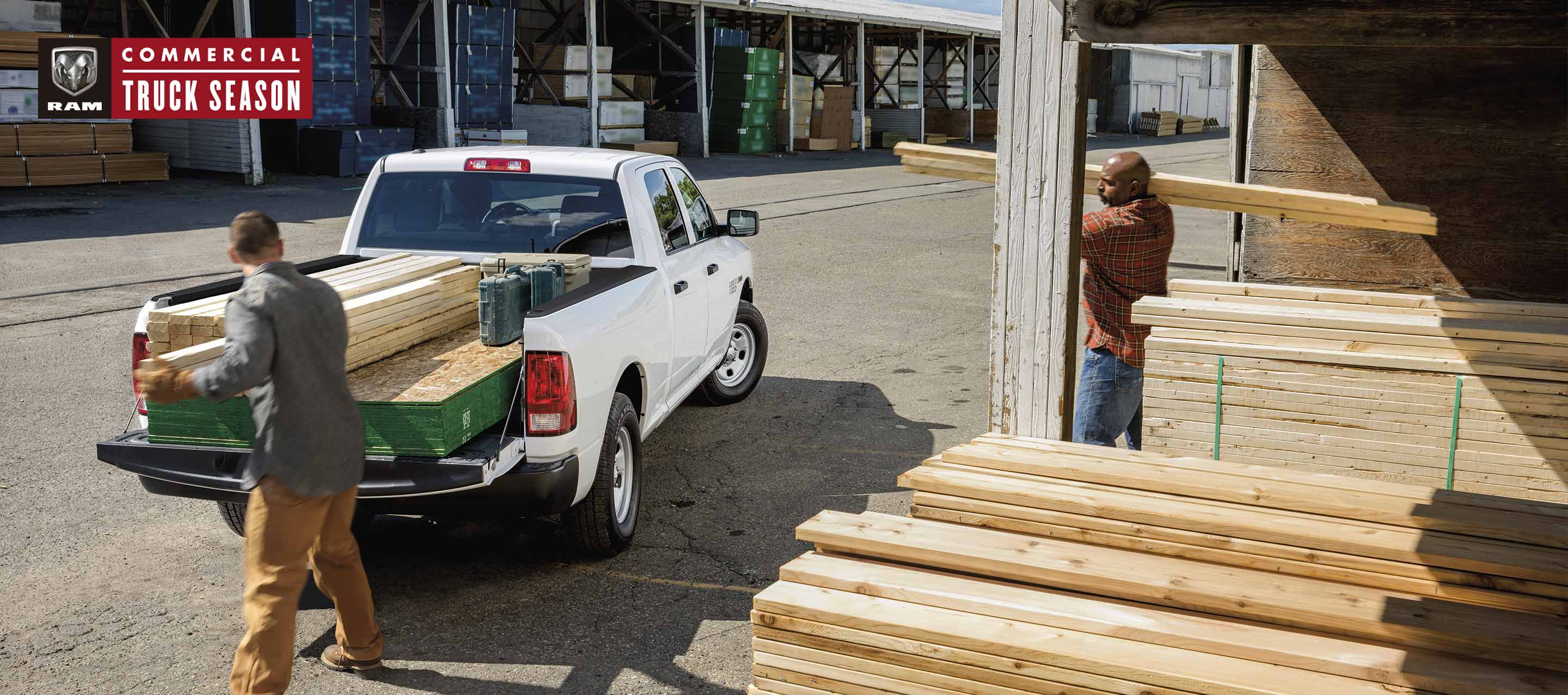A man loading lumber into the pickup bed of a white 2023 Ram 1500 Classic Tradesman 4x4 Crew Cab. Ram Commercial Truck Season.