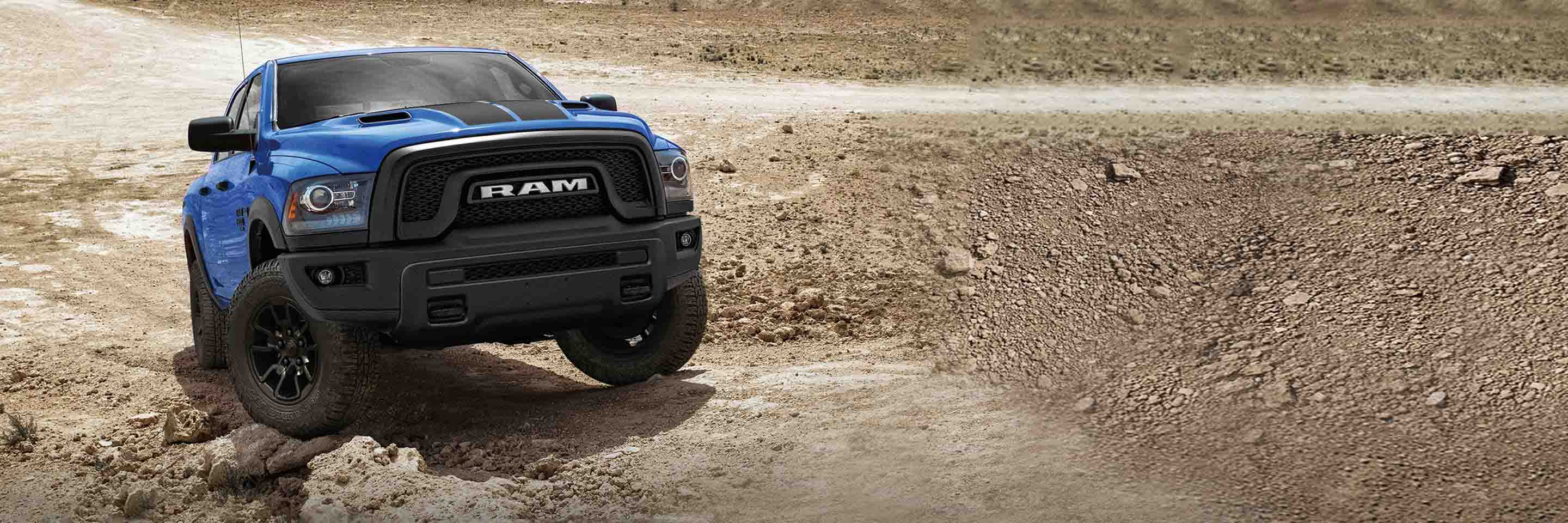 A blue 2023 Ram 1500 Classic Warlock 4x4 Crew Cab with the All-Terrain Package, climbing a sloping, rocky trail, off-road.