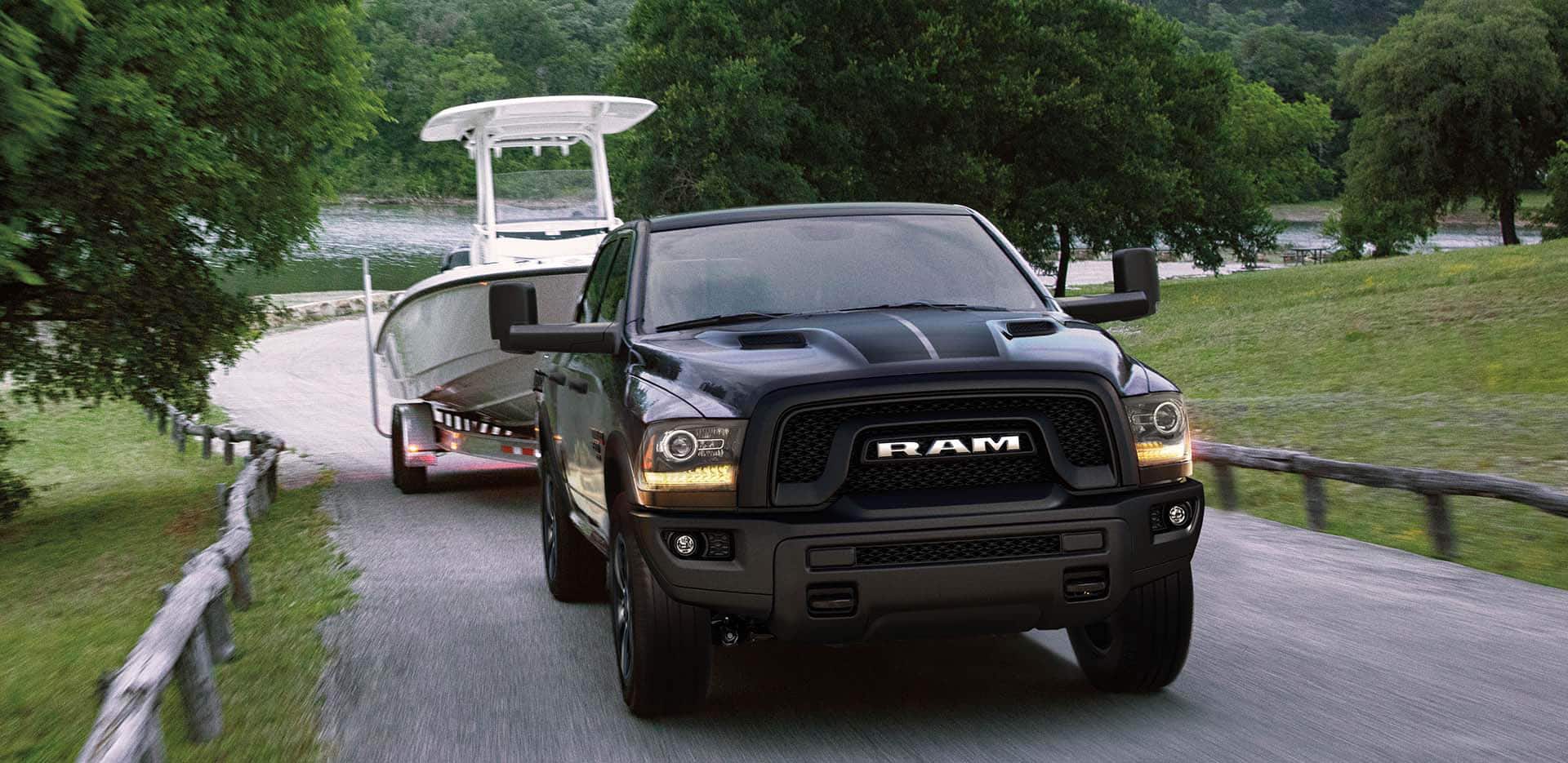 Display A head-on view of a 2023 Ram 1500 Classic Warlock 4x4 Crew Cab,  towing a boat  as it exits the launch site of a lake.