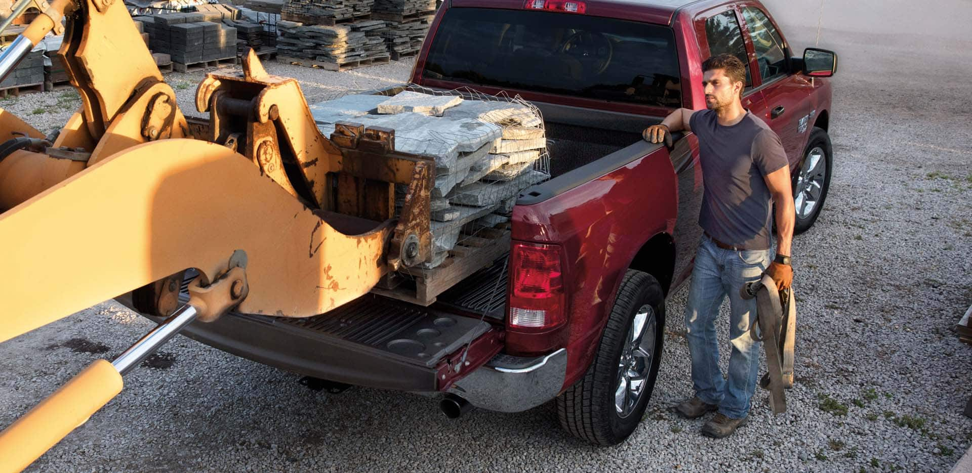 Display A man supervising as a forklift loads a pallet of paving stones into the bed of a red 2023 Ram 1500 Classic Tradesman 4x4 Crew Cab.