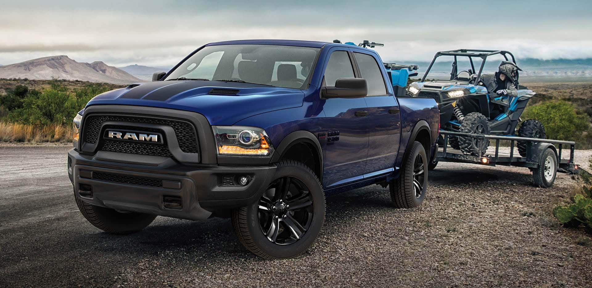 Display A blue 2023 Ram 1500 Classic Warlock 4x4 Crew Cab hitched to a flatbed trailer with an ATV on it which is about to be removed.