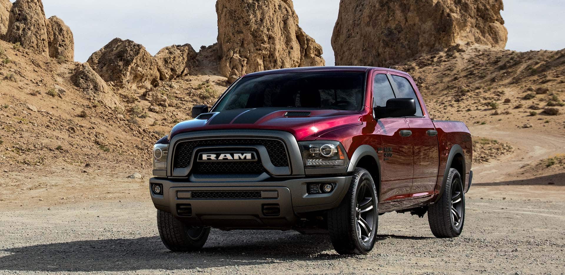 Display A red 2023 Ram 1500 Classic Warlock 4x4 Crew Cab parked on a twisting desert road with rocky outcroppings in the distance.