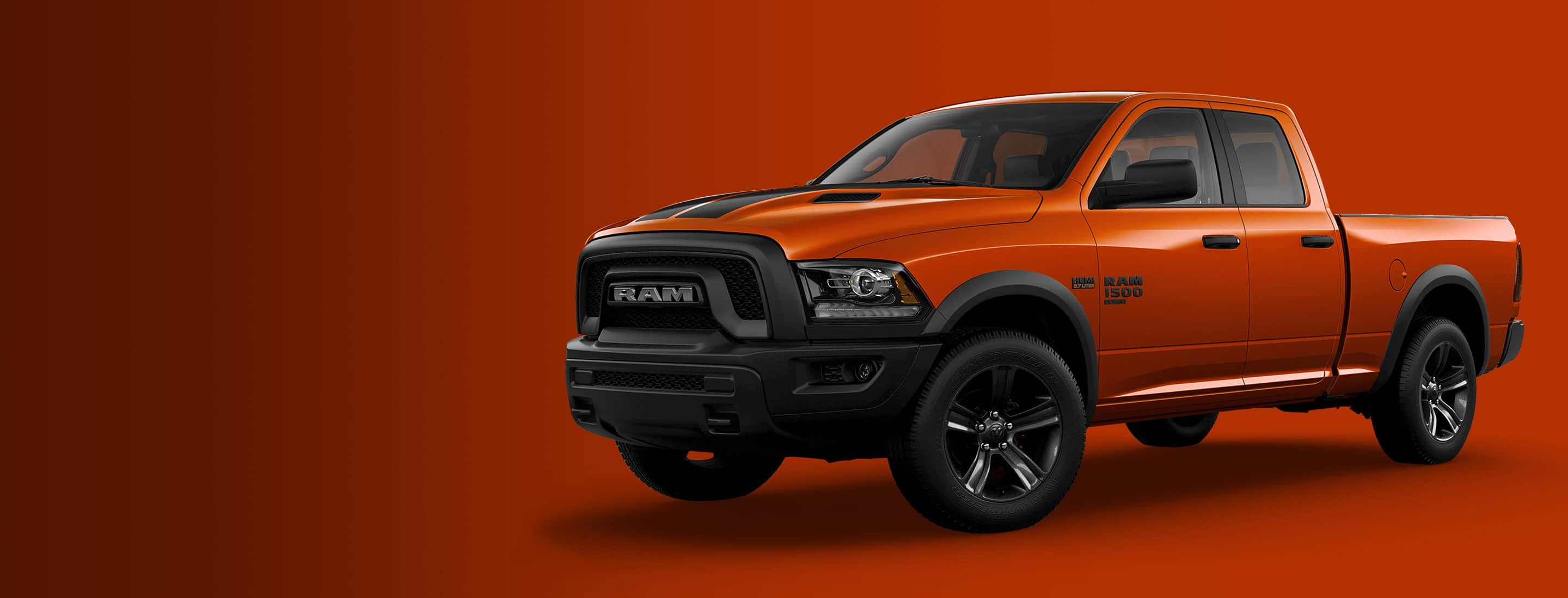 A driver-side angled profile of a bright orange 2023 Ram 1500 Classic Warlock Harvest Special Edition Quad Cab on a bright orange background.