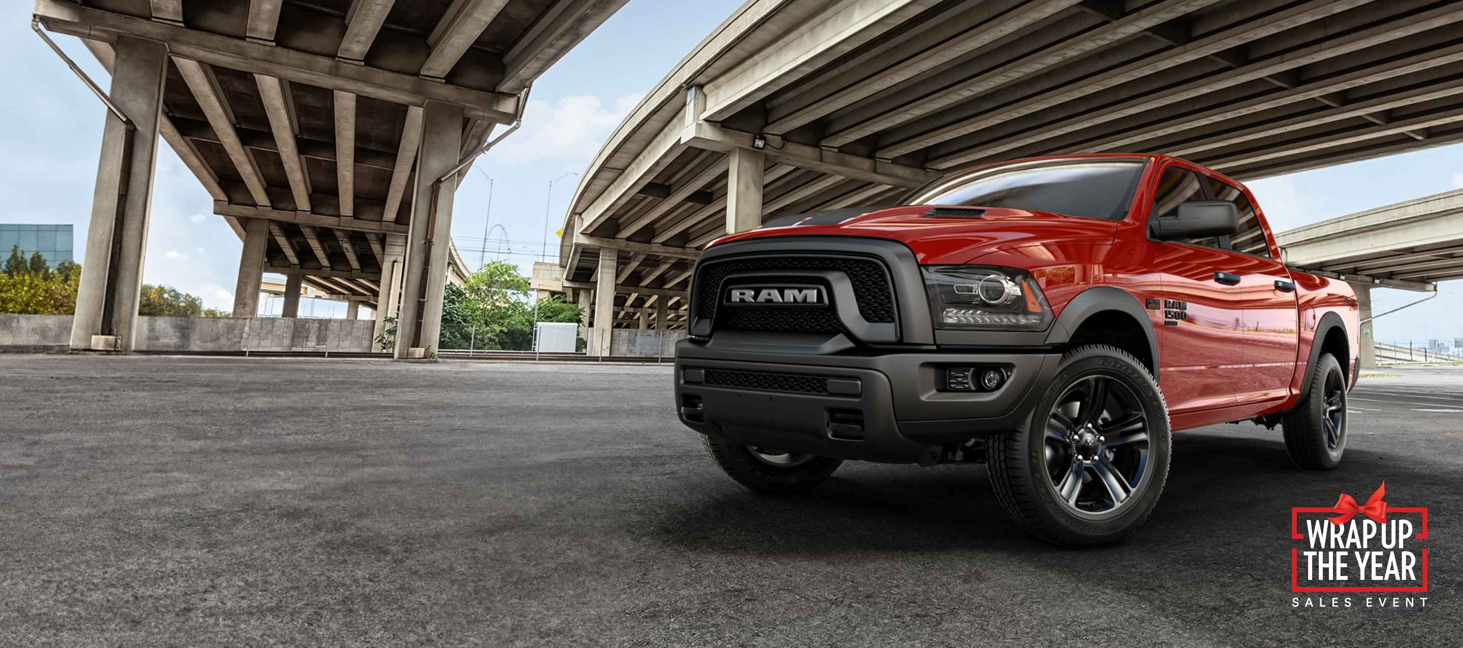 A red 2023 Ram 1500 Classic Warlock 4x4 Crew Cab parked under a group of freeway overpasses. Ram Wrap Up the Year Sales Event.
