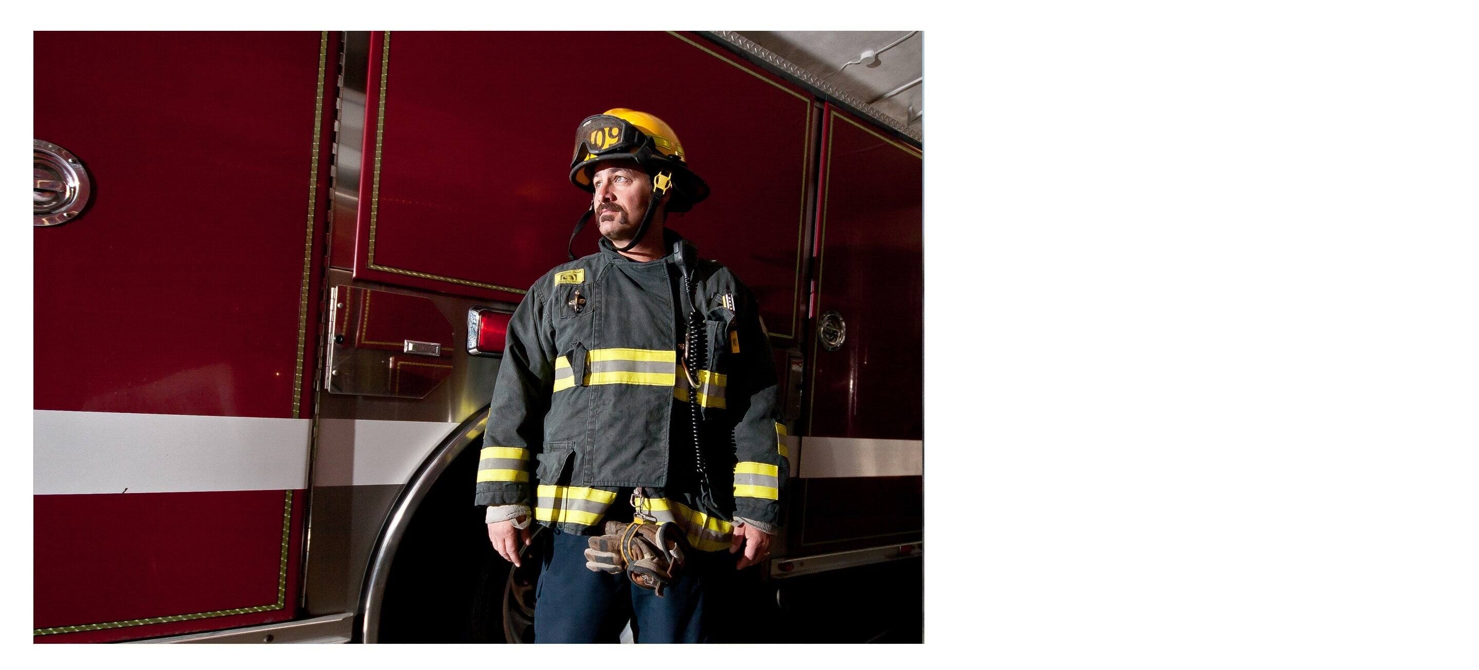 A firefighter in full gear, standing beside a large fire truck.