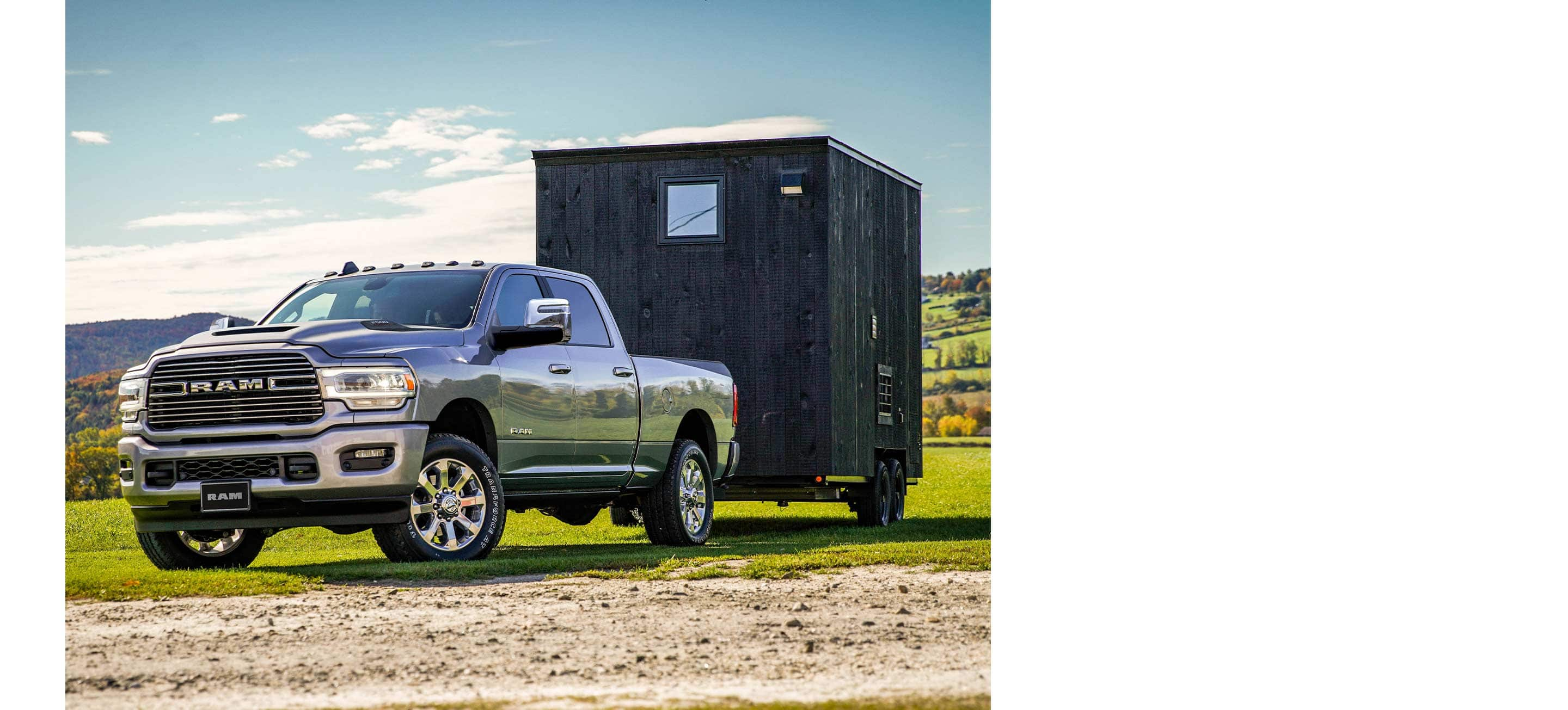 A 2023 Ram 2500 Laramie Crew Cab towing a small trailer down a country road.