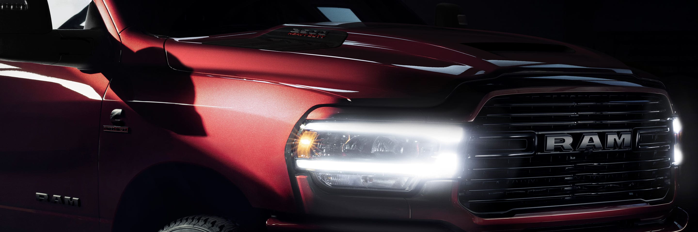 An angled front end close-up of the 2023 Ram 2500 Laramie with its headlamps on, in a dark studio.