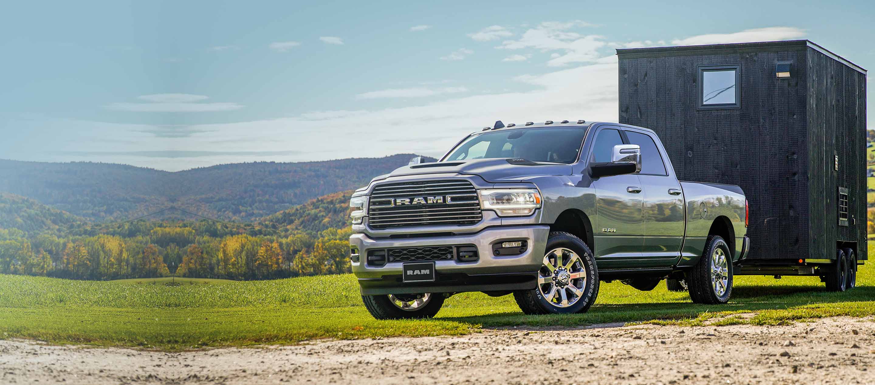 A 2023 Ram 2500 Laramie 4x4 Crew Cab towing a trailer parked on a grassy trail off-road. 