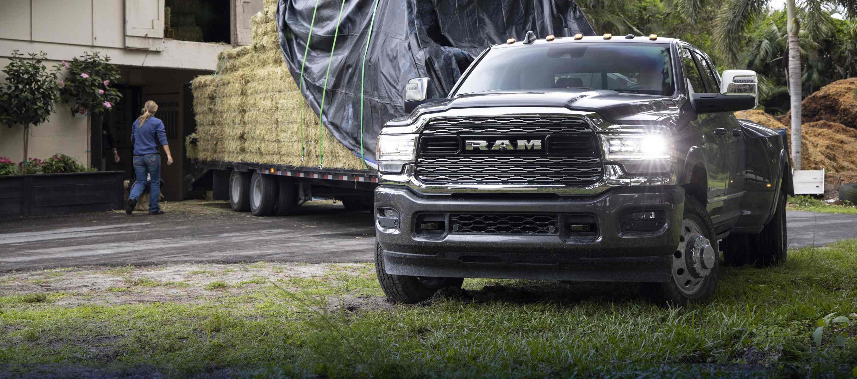 A gray 2023 Ram 3500 Limited 4x4 Mega Cab towing a flatbed trailer loaded high with bales of hay. 
