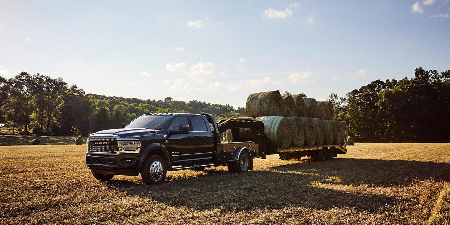 A 2023 Ram Chassis Cab being driven through an open field with a gooseneck trailer full of several bales of hay.