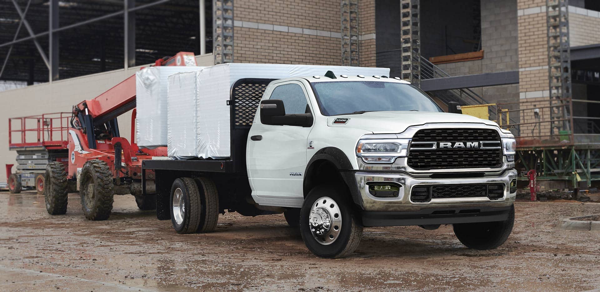 Display A 2023 Ram Chassis Cab with a platform upfit loaded with building materials, parked at a commercial construction site.
