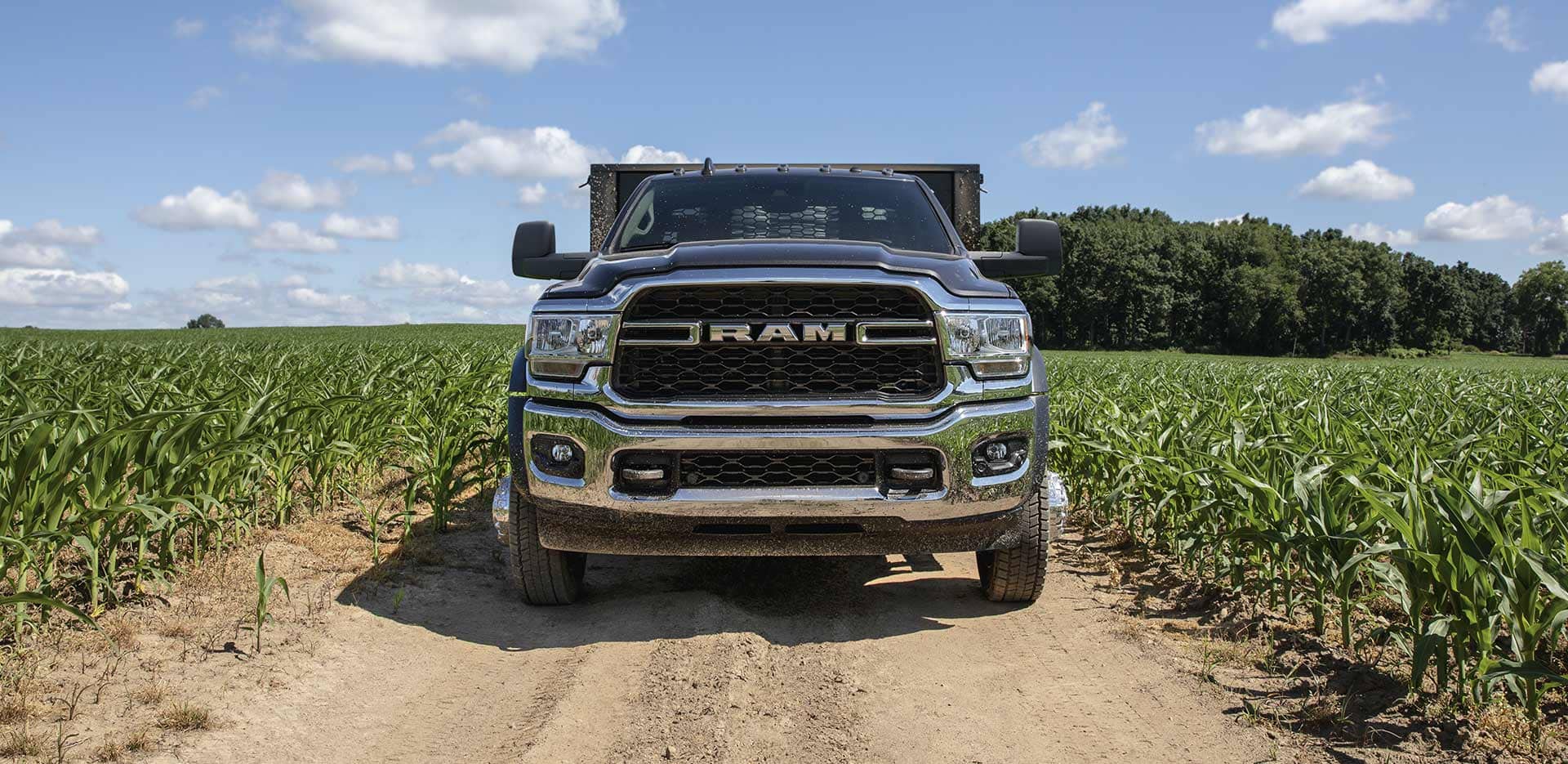Display The 2023 Ram Chassis Cab with a stake bed upfit on a dirt road between fields of crops.