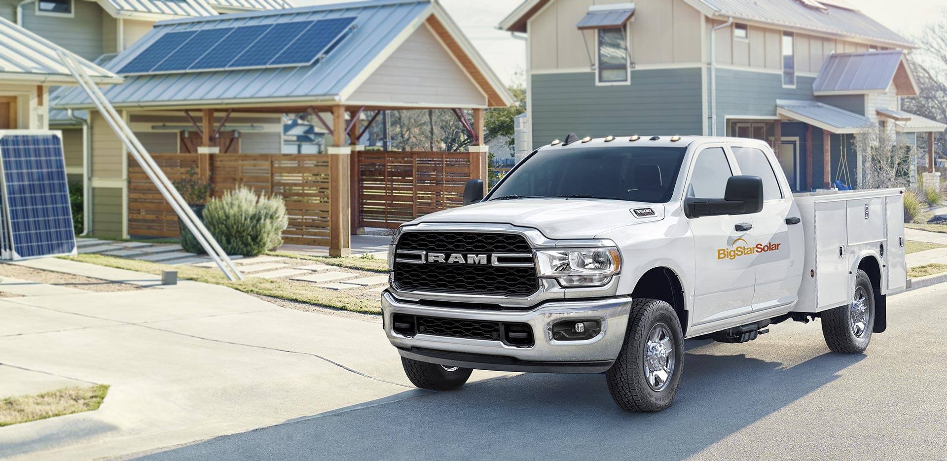 Display The 2023 Ram Chassis Cab with a solar company logo on its side, parked in front of a home with solar panels on the garage roof.