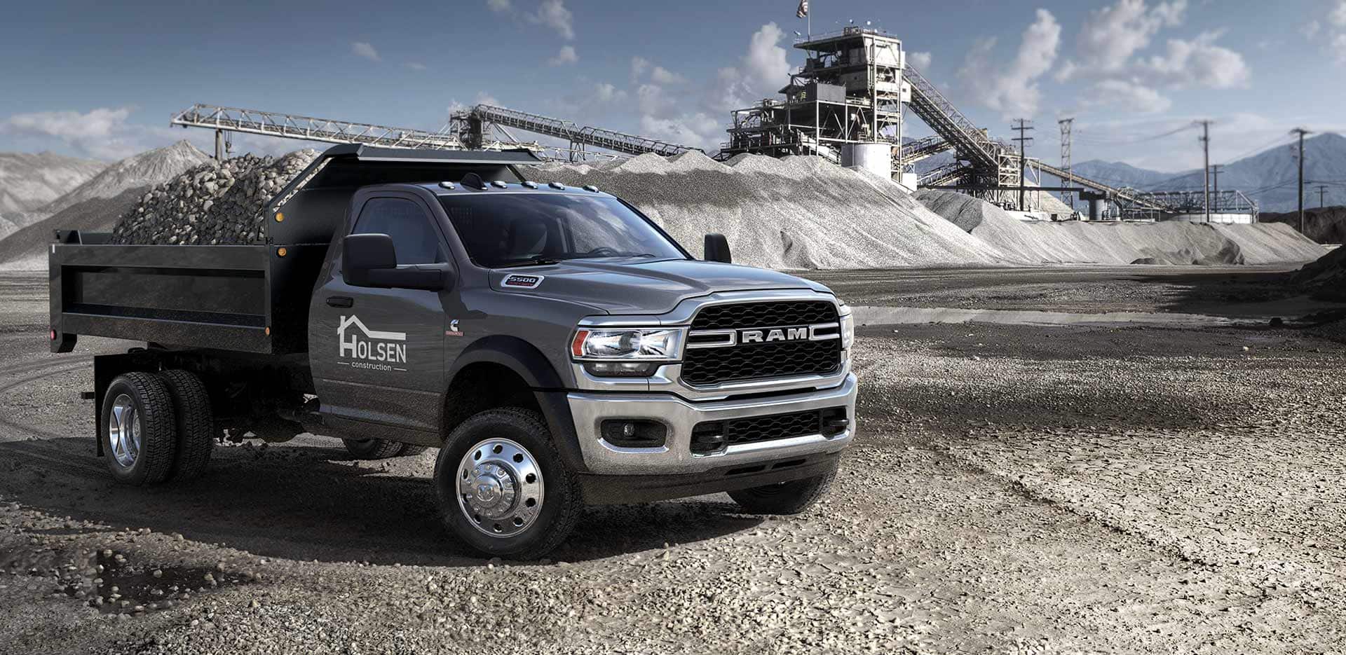 Display A 2023 Ram Chassis Cab with a dump body upfit loaded with gravel and a construction company name and logo on the passenger-side door.