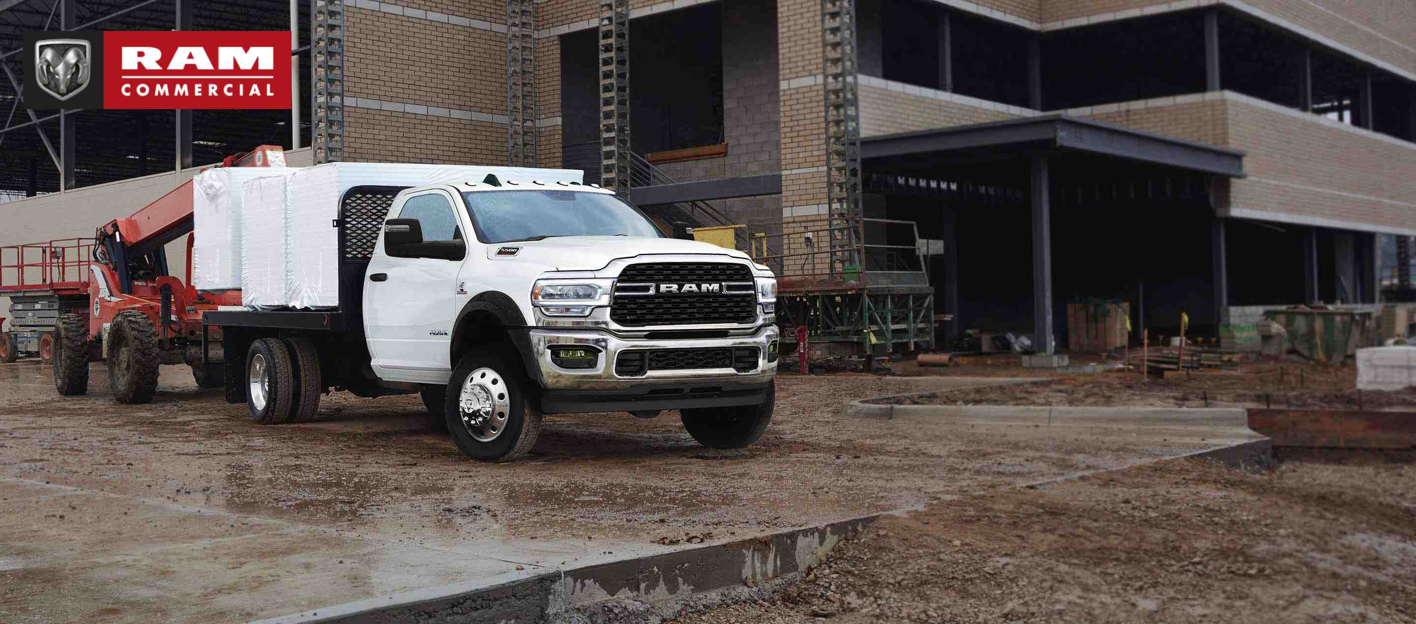 A 2023 Ram Chassis Cab with a platform upfit loaded with building materials, parked at a commercial construction site. Ram Commercial.