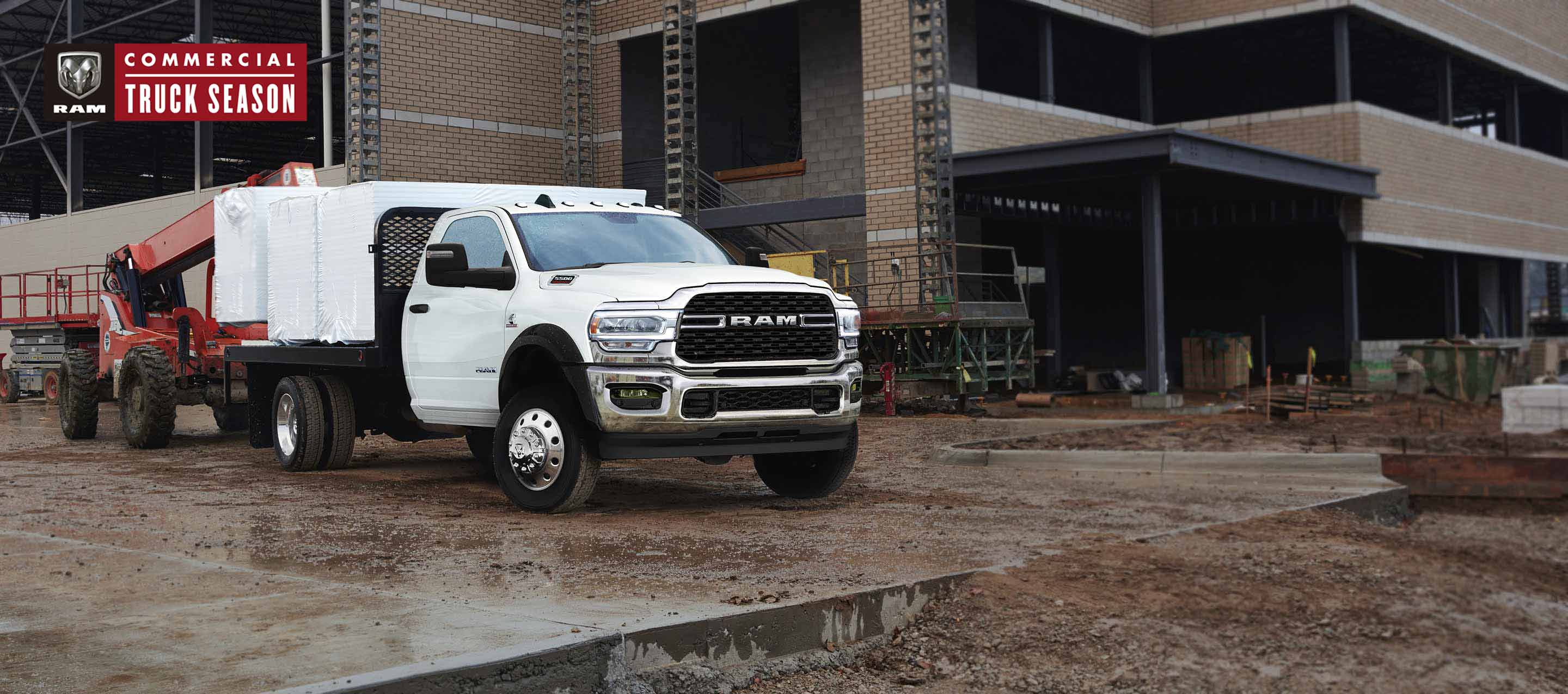 A 2023 Ram Chassis Cab with a platform upfit loaded with building materials, parked at a commercial construction site.