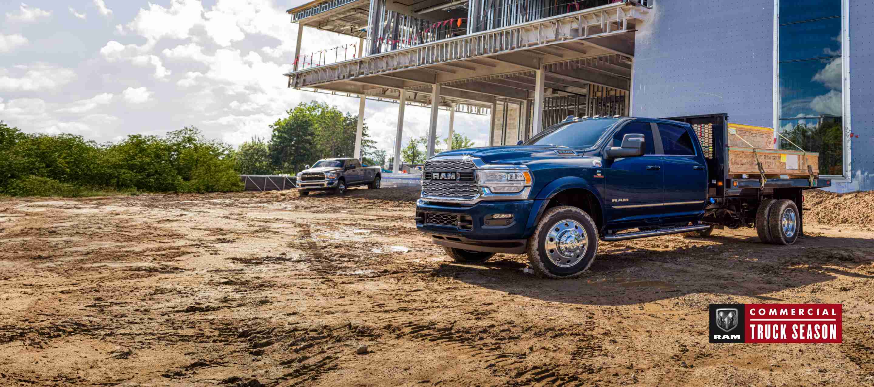 A blue 2023 Ram 5500 Limited Chassis Cab 4x4 Crew Cab with utility bed upfit, parked at a commercial building site. Ram Commercial Truck Season.