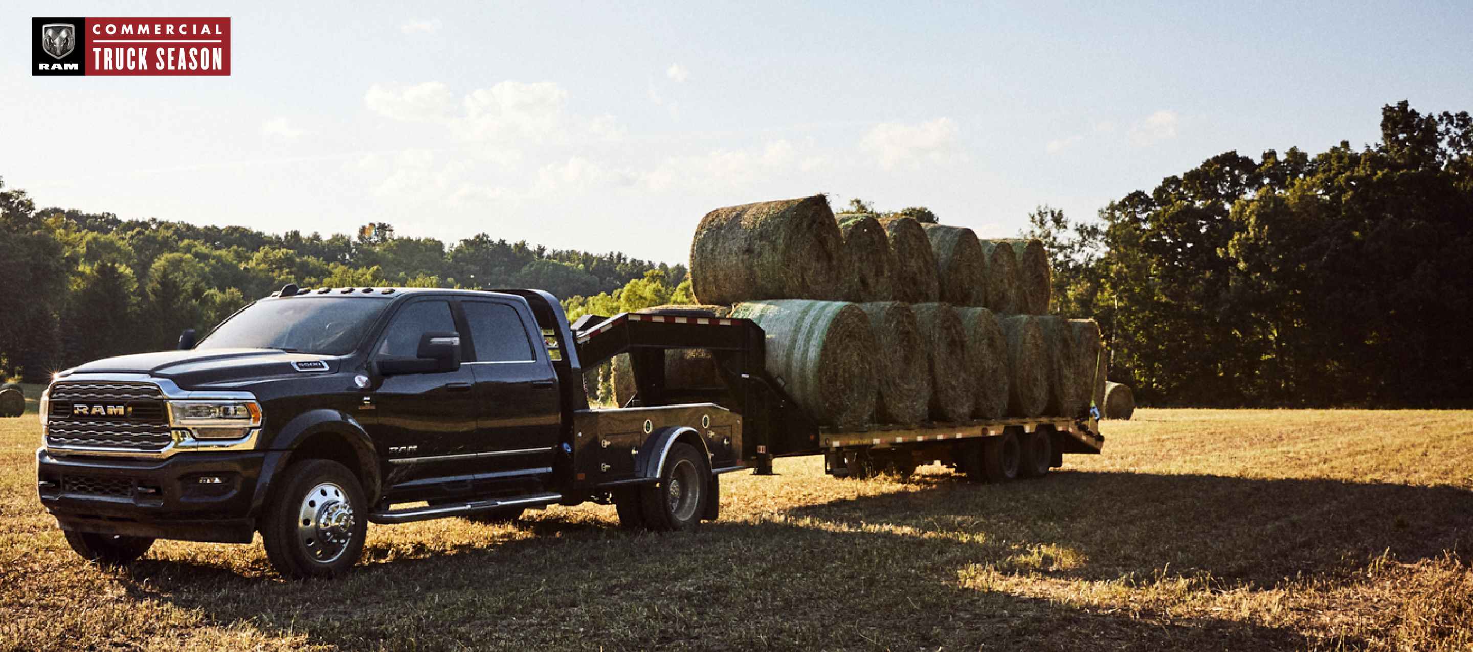 A black 2023 Ram 5500 Limited Chassis Crew Cab parked in a field with a Rancher Upfit carrying a dozen large bales of hay. Ram Commercial Truck Season.
