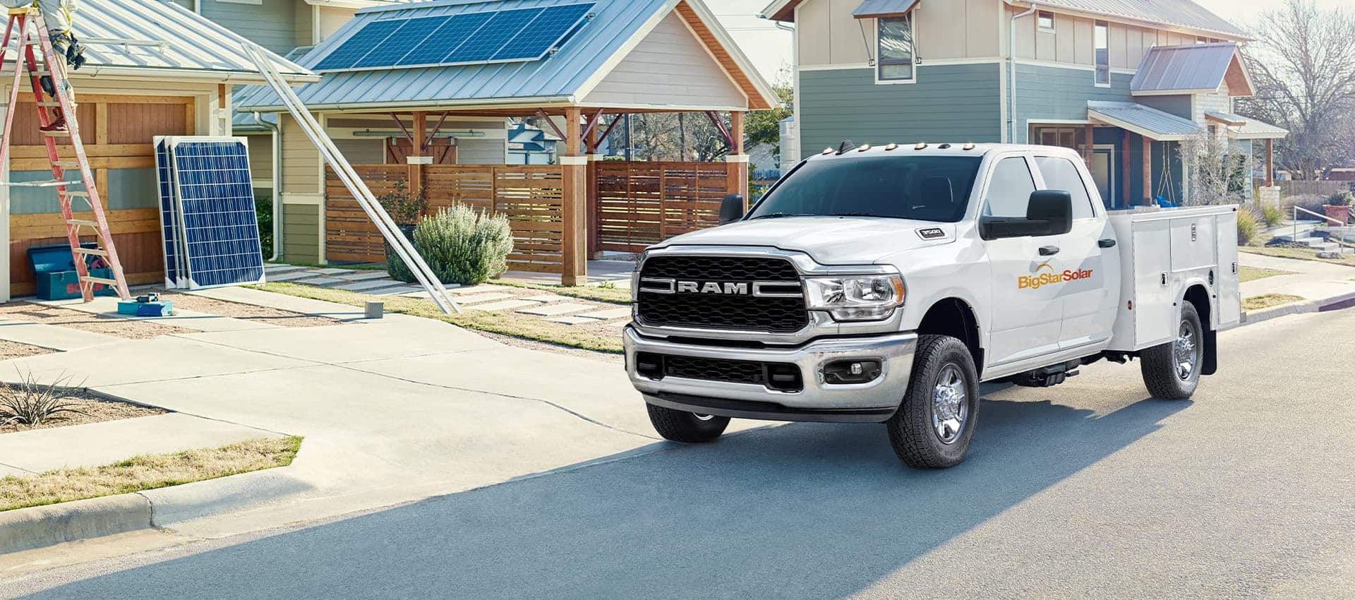The 2023 Ram Chassis Cab with a solar company logo on its side, parked in front of a home with solar panels on the garage roof.