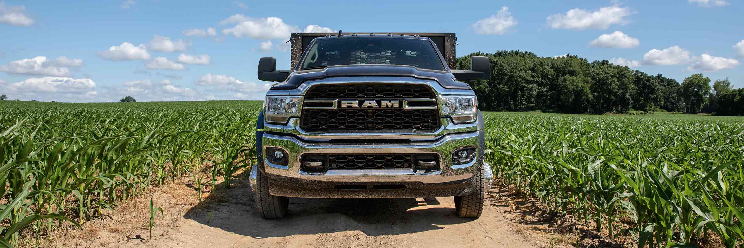 A head-on view of a 2023 Ram Chassis Cab being driven on a dirt road with farm fields on both sides.