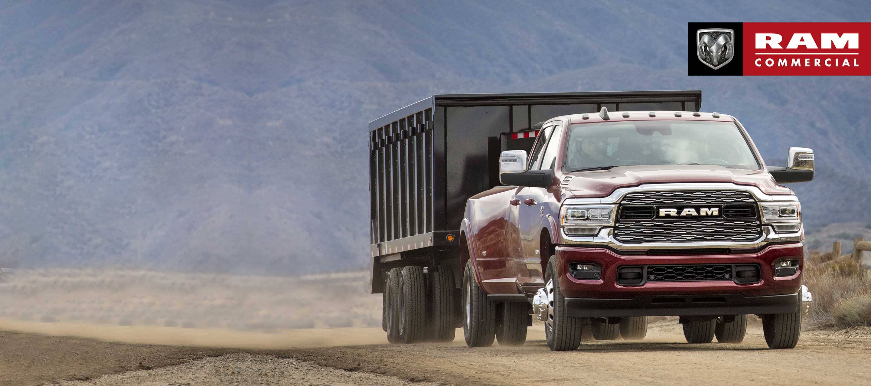 A 2023 Ram 3500 Limited towing a dump body trailer on a dirt road with mountains in the distance.