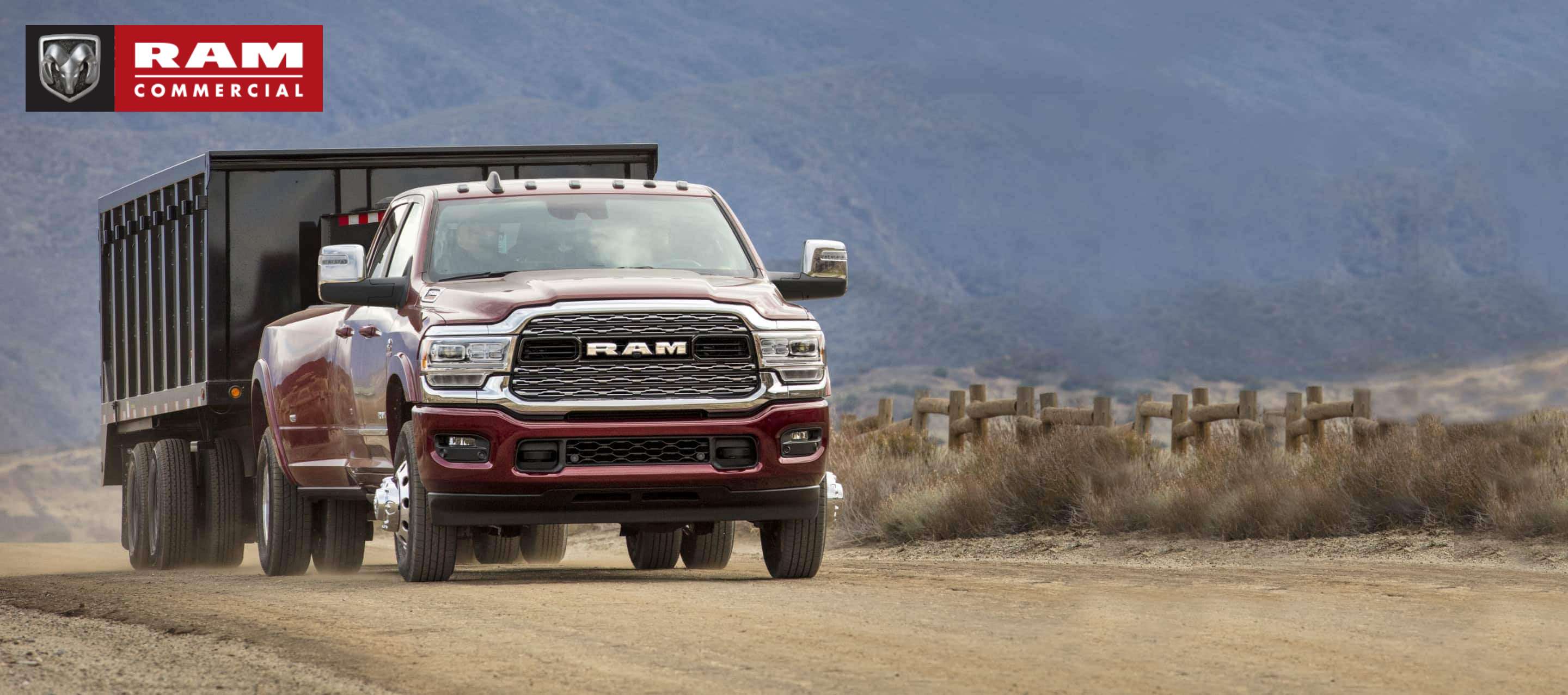 A 2023 Ram 3500 Limited towing a dump body trailer on a dirt road with mountains in the distance. Ram Commercial.