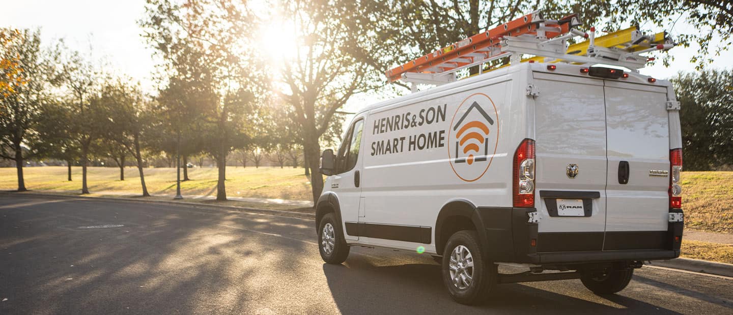 A 2023 Ram ProMaster with ladders on its roof rack and the logo of a smart home installation company on its side.