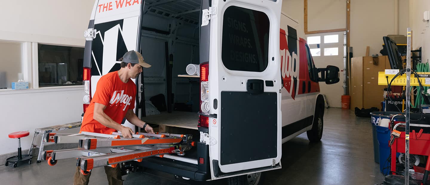 A man guiding a ladder into a storage compartment on the floor of a 2023 Ram ProMaster.