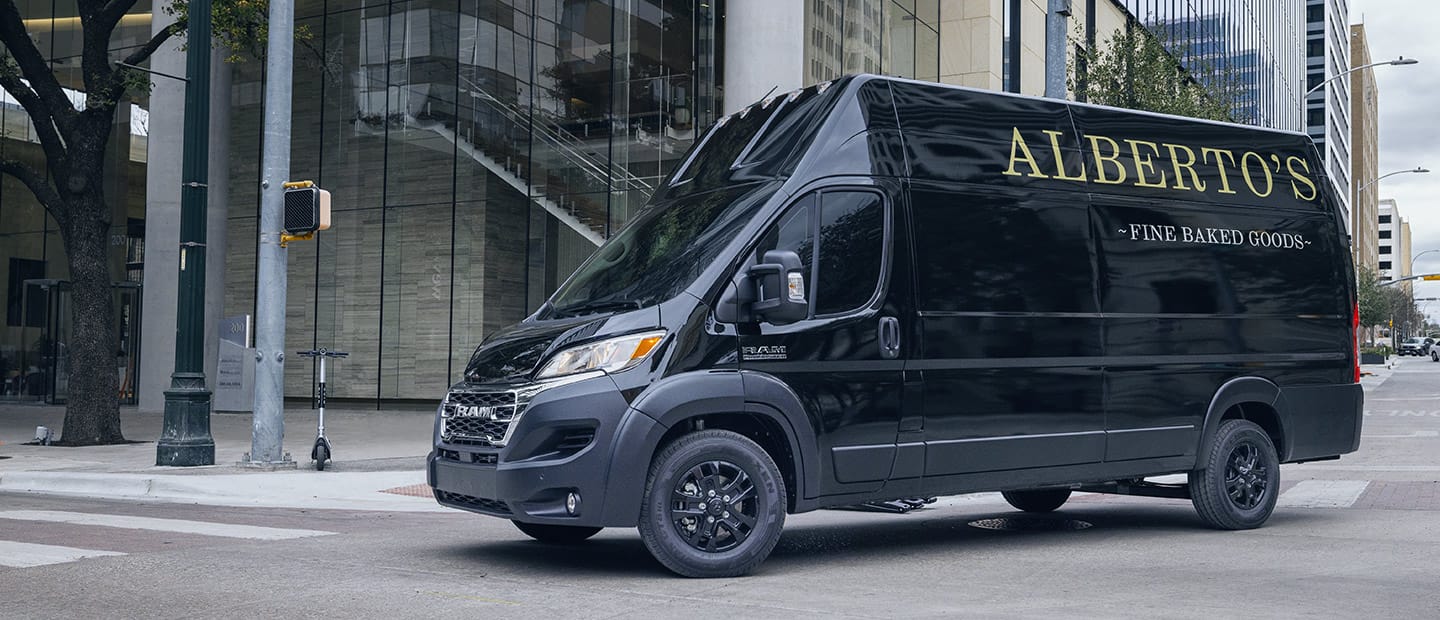 A 2023 Ram ProMaster 3500 Cargo Van new Super High Roof with a bakery logo on its side being driven in the city.