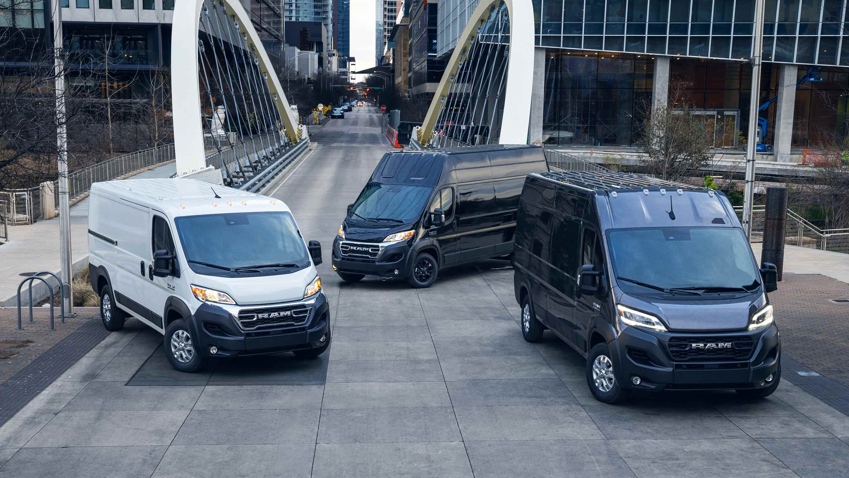 Display Three 2023 Ram ProMaster Vans parked on city street: a 1500 Cargo Van, a 3500 Cargo Van Super High Roof and a 2500/3500 Cargo Van High Roof.