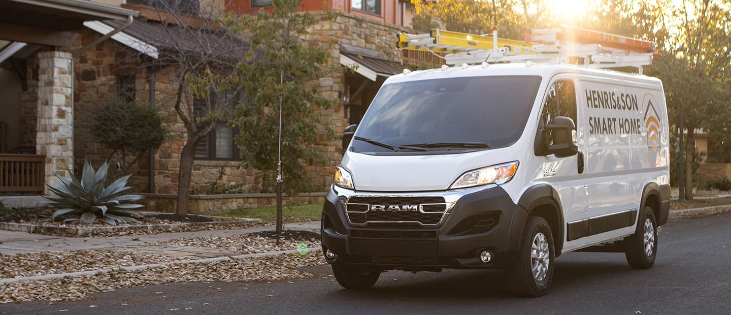The 2023 Ram ProMaster 1500 Cargo Van with two ladders on its roof rack and the logo of a smart home installation company on its side.