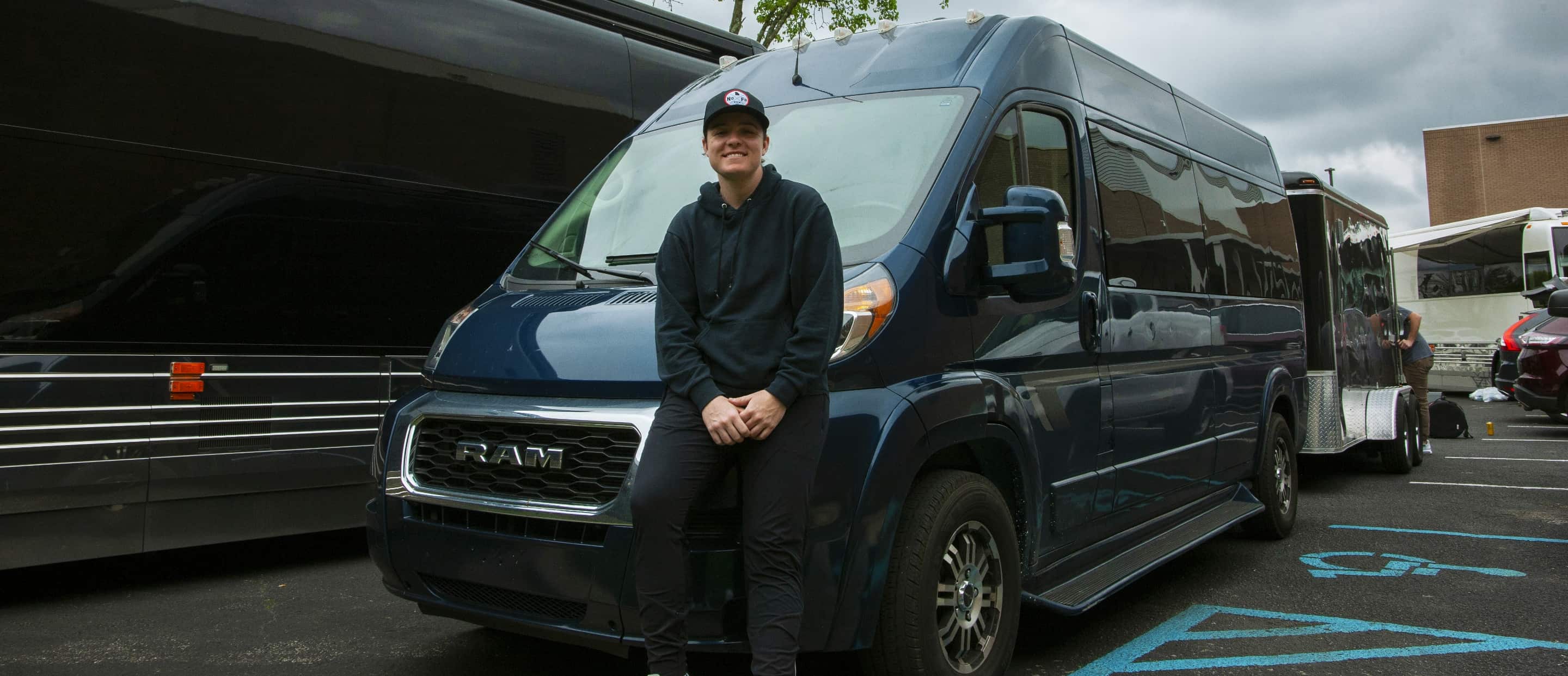 Country Artist Lily Rose leaning on the front end of the Ram ProMaster 2500 BandVan Window Van High Roof, connected to a trailer.