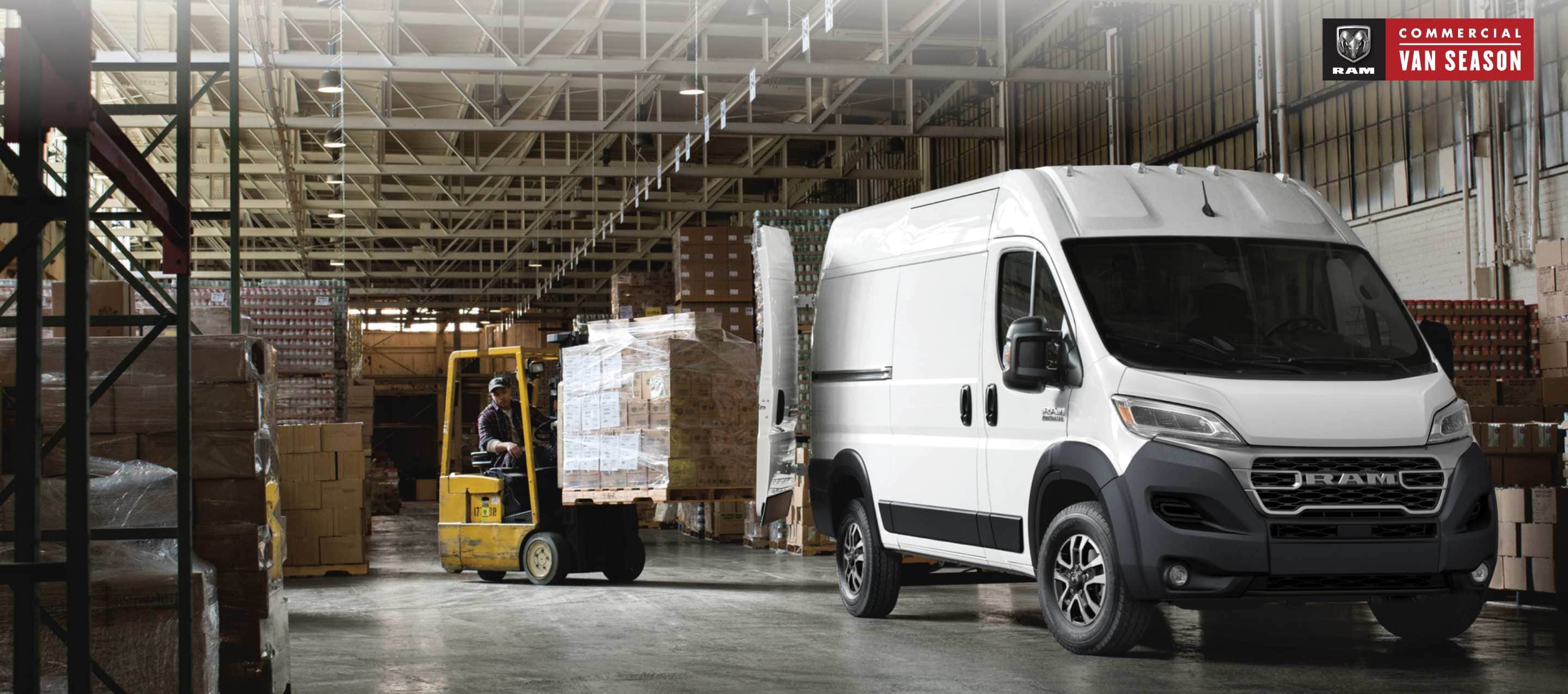 An angled front profile of a white 2023 Ram ProMaster 1500 High Roof Cargo Van, with its rear doors fully open and a forklift with a pile of boxes being driven toward the back of the van. Ram Commercial Van Season.