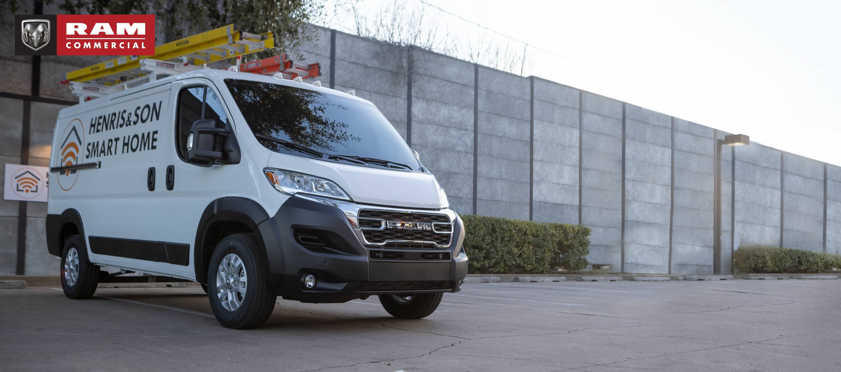 A white 2023 Ram ProMaster 1500 Low Roof Cargo Van with security company signage on its side, parked beside a commercial building. Ram Commercial.