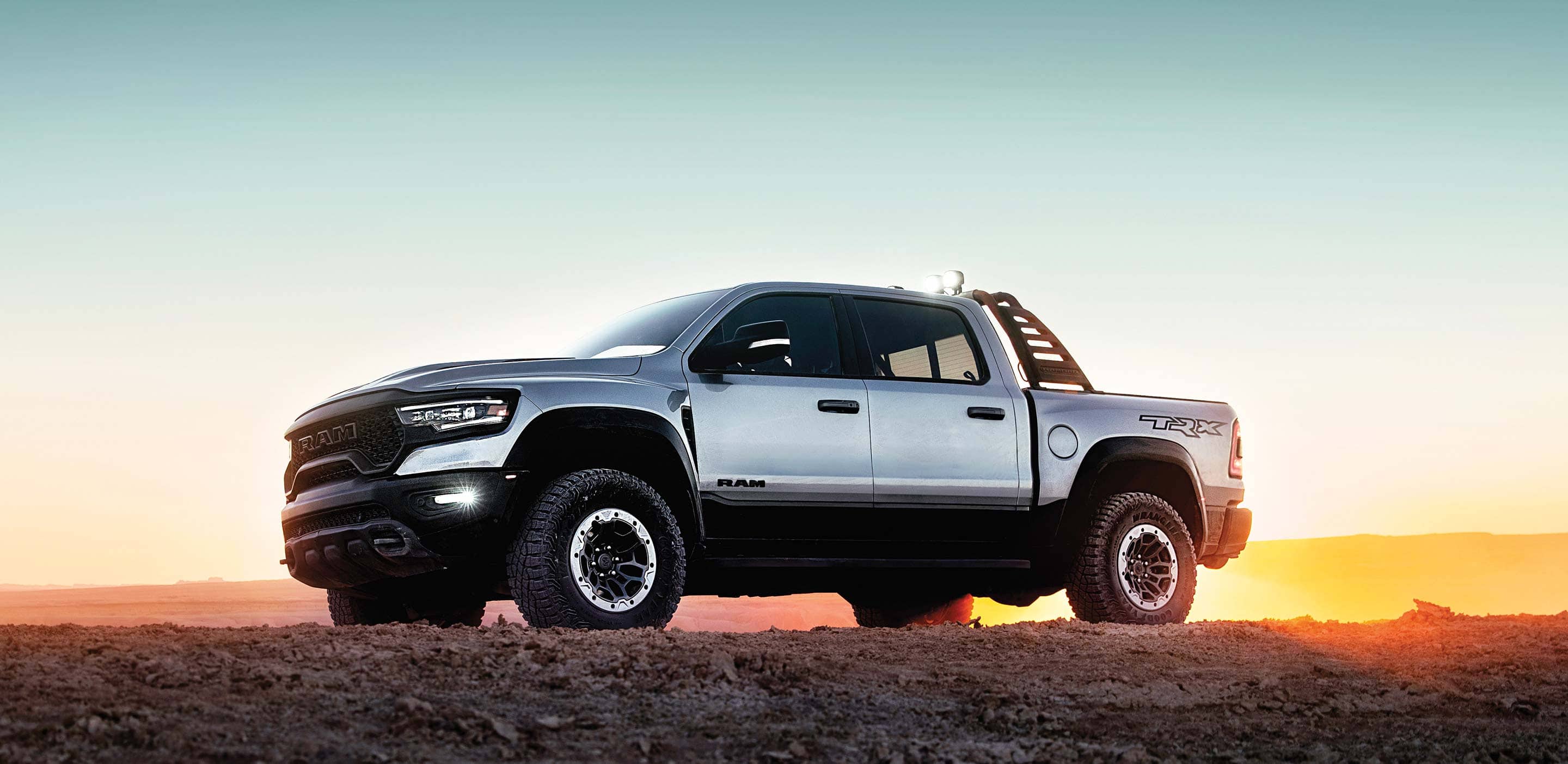 Display A side profile of the 2023 Ram 1500 TRX, parked in the desert with the sun setting behind it.