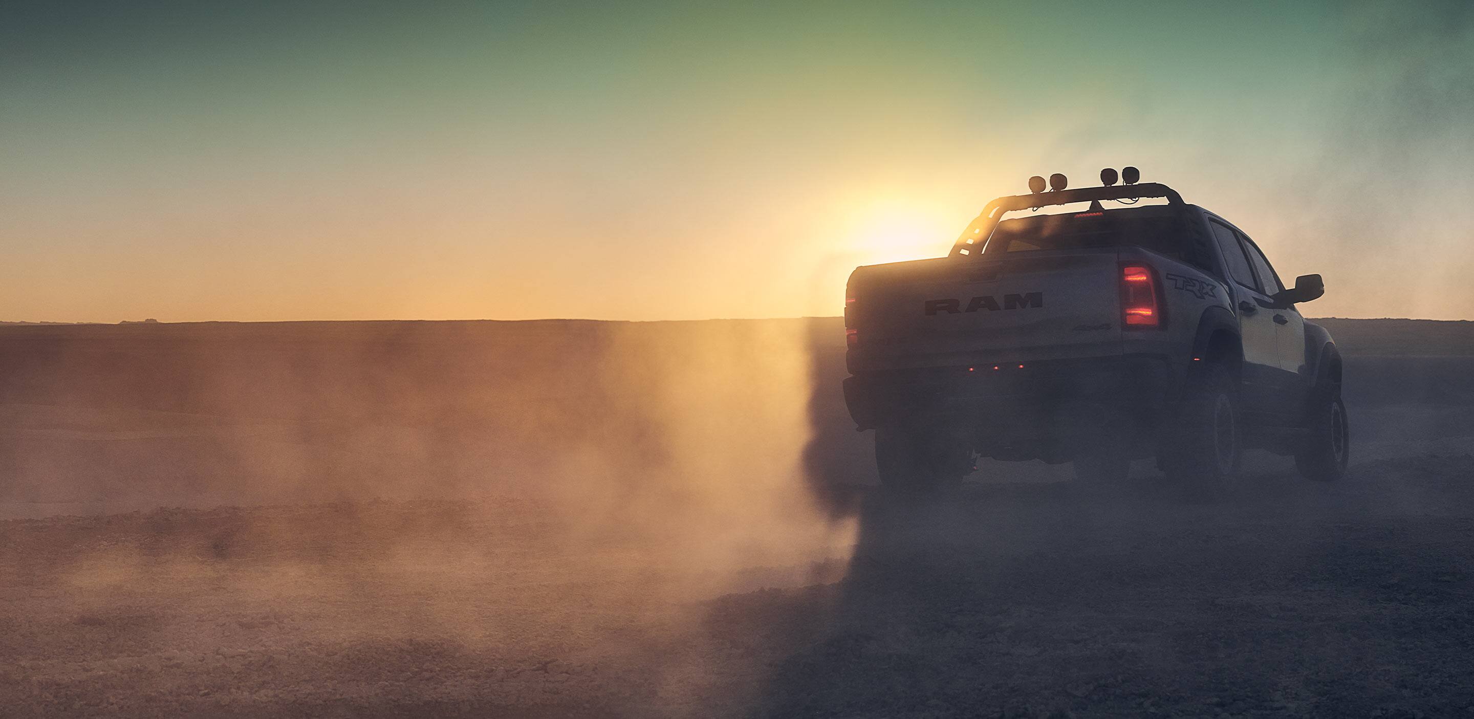 Display The 2023 Ram 1500 TRX with its taillamps on as it is driven into the sunset.