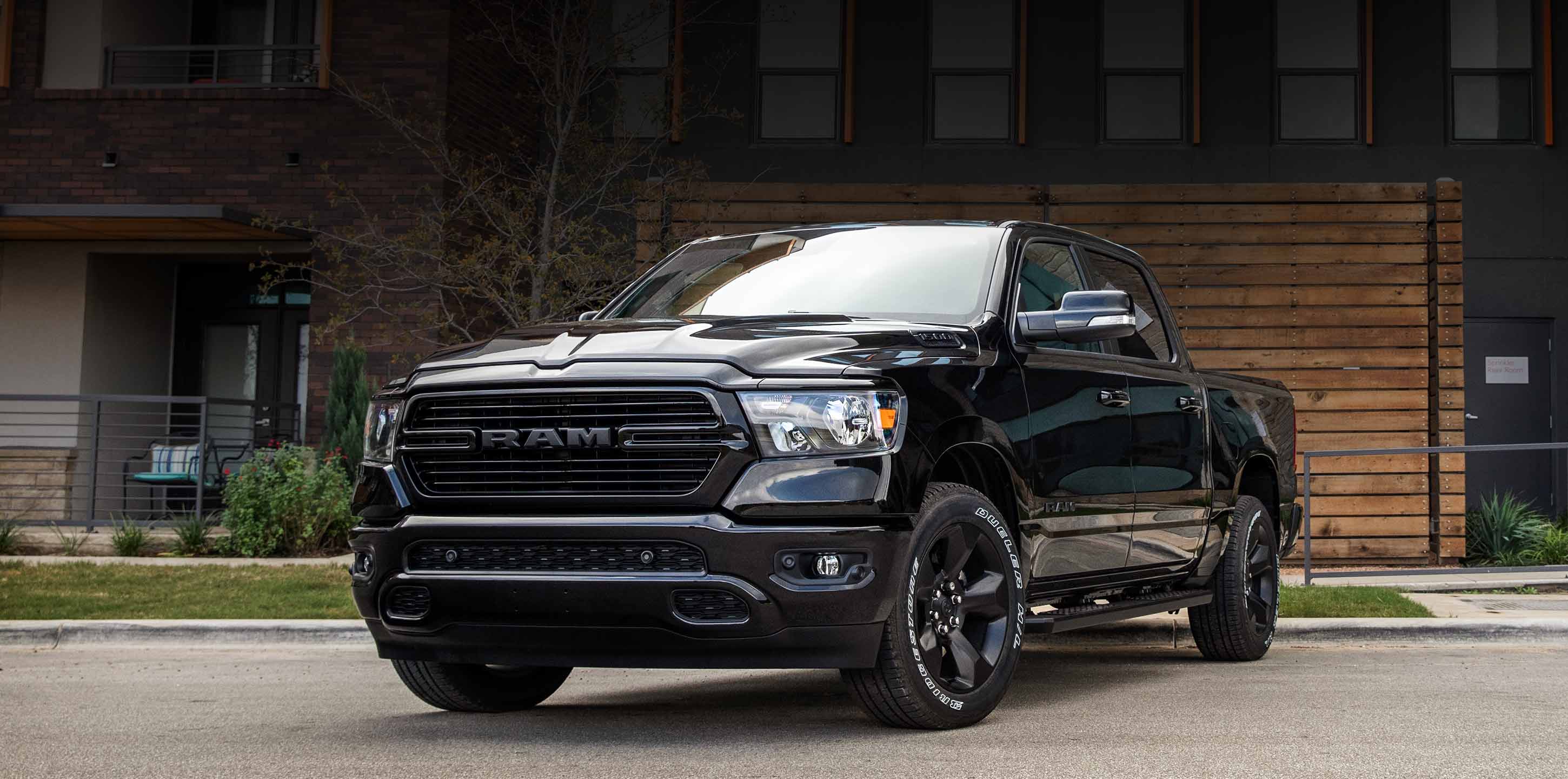 A front angled driver-side profile of a black 2024 Ram 1500 Laramie Crew Cab parked in front of an apartment complex.