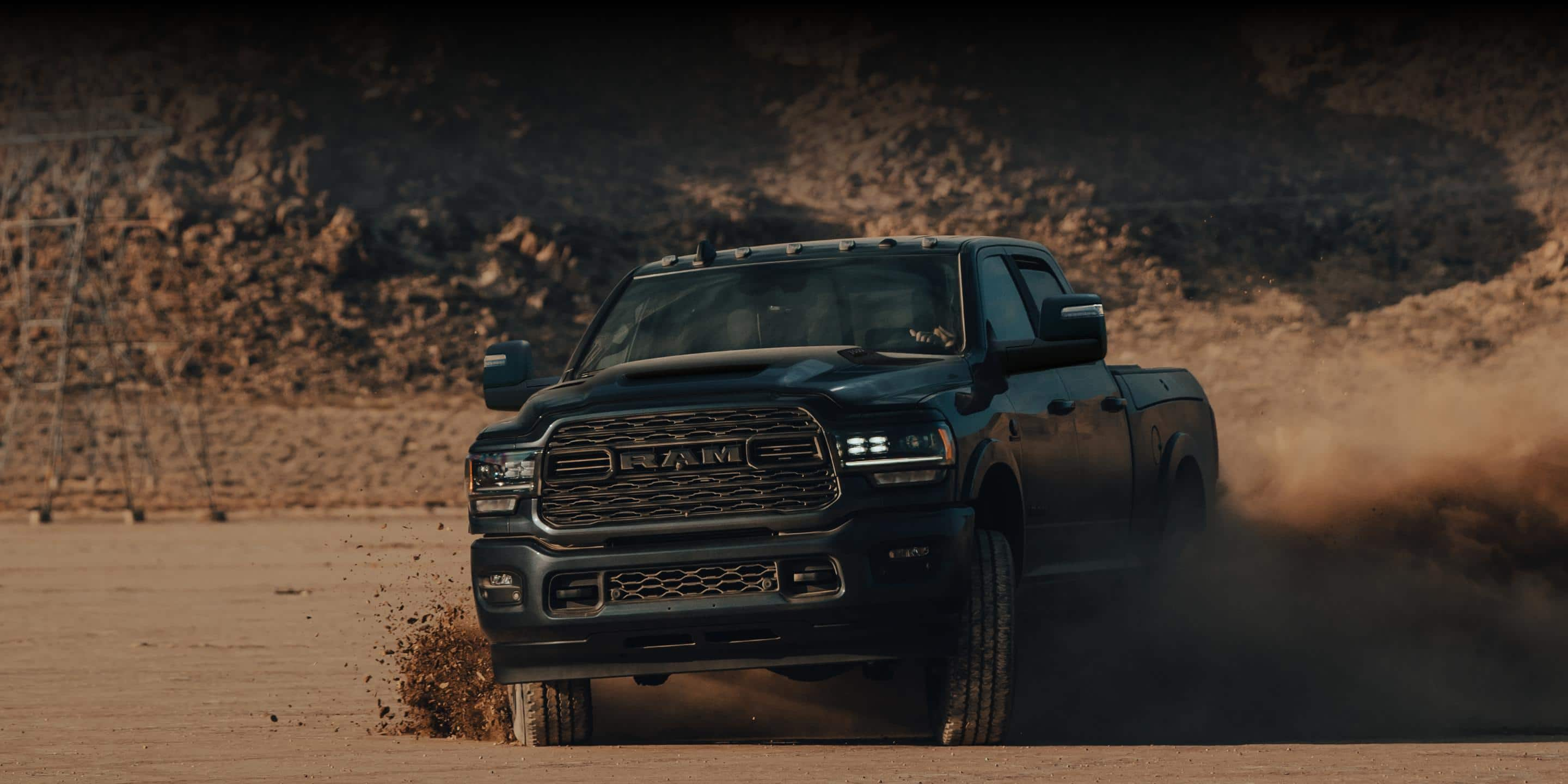 A 2024 Ram 2500 Limited Crew Cab being driven on a sandy clearing off-road, kicking up dust with its tires.